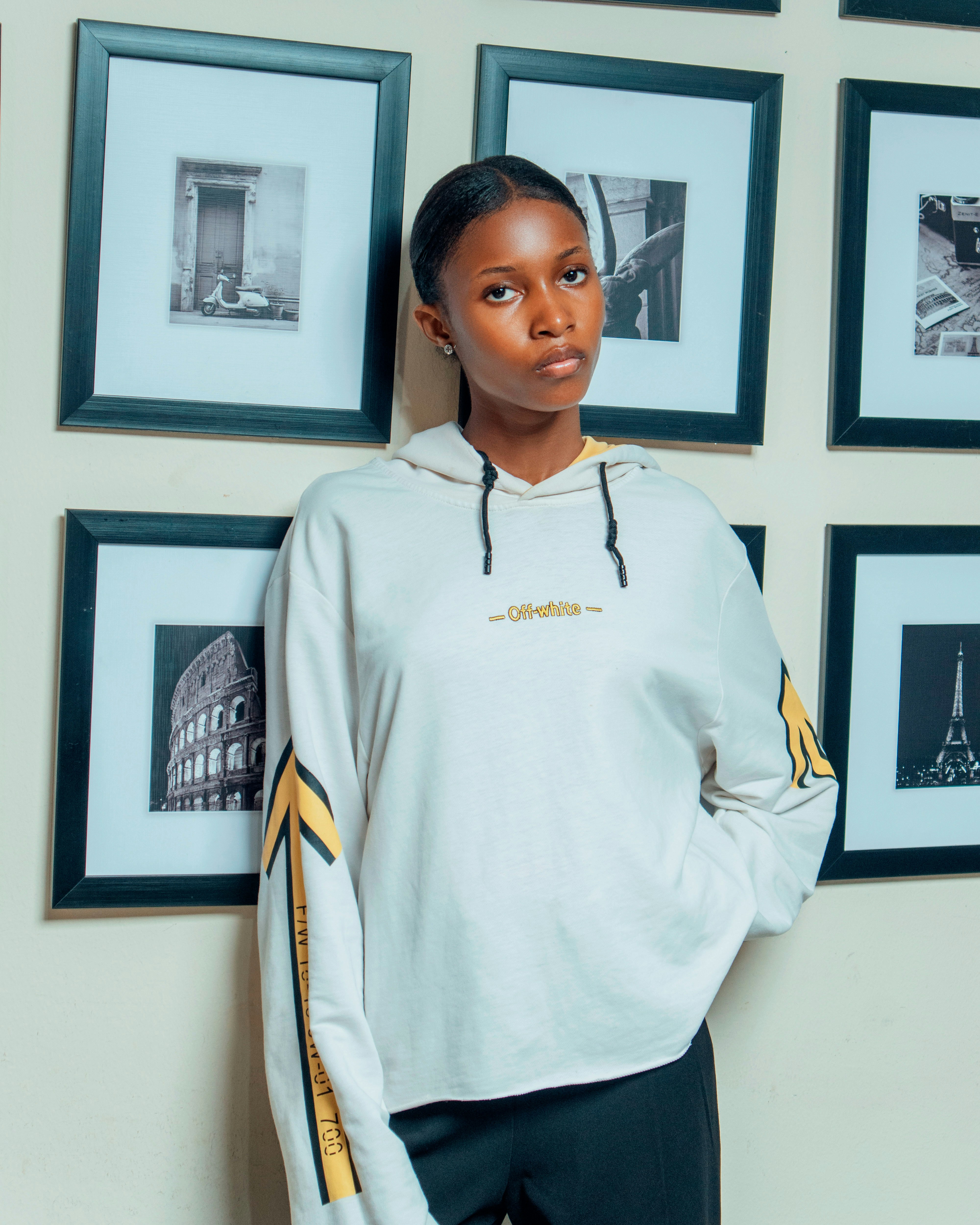 Young woman in hoodie stands against framed artwork