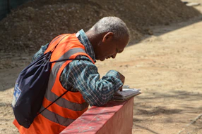 Man in orange vest writing on paper outdoors