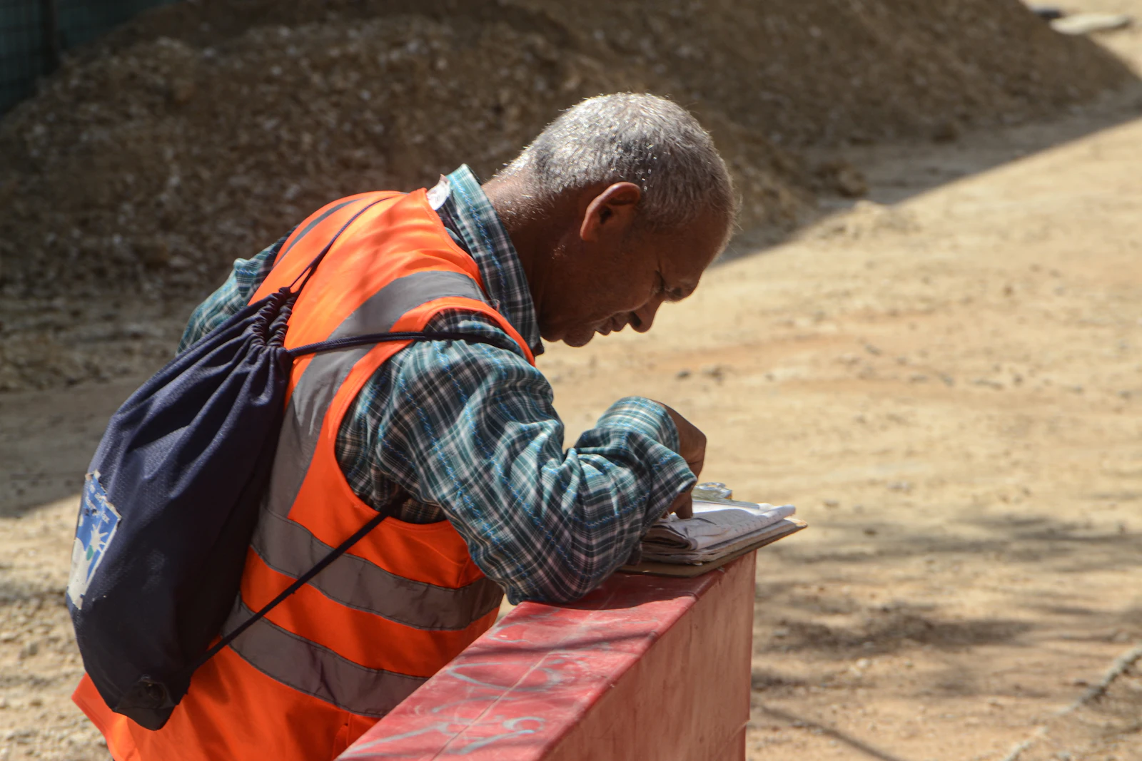 Profissional de colete laranja de segurança conferindo anotações em caderno ao ar livre em canteiro de obras
