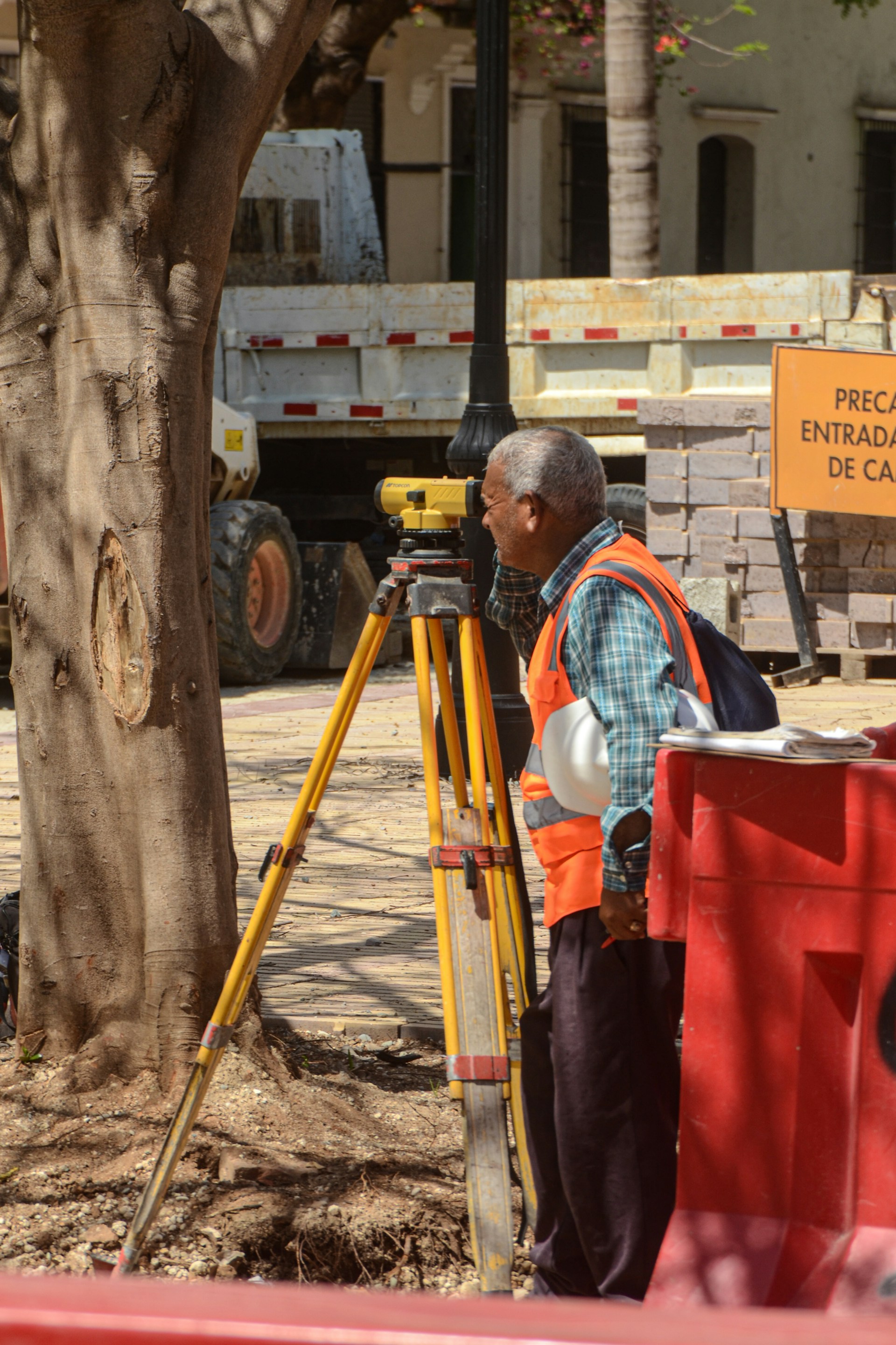 Man in orange vest uses surveying equipment outdoors