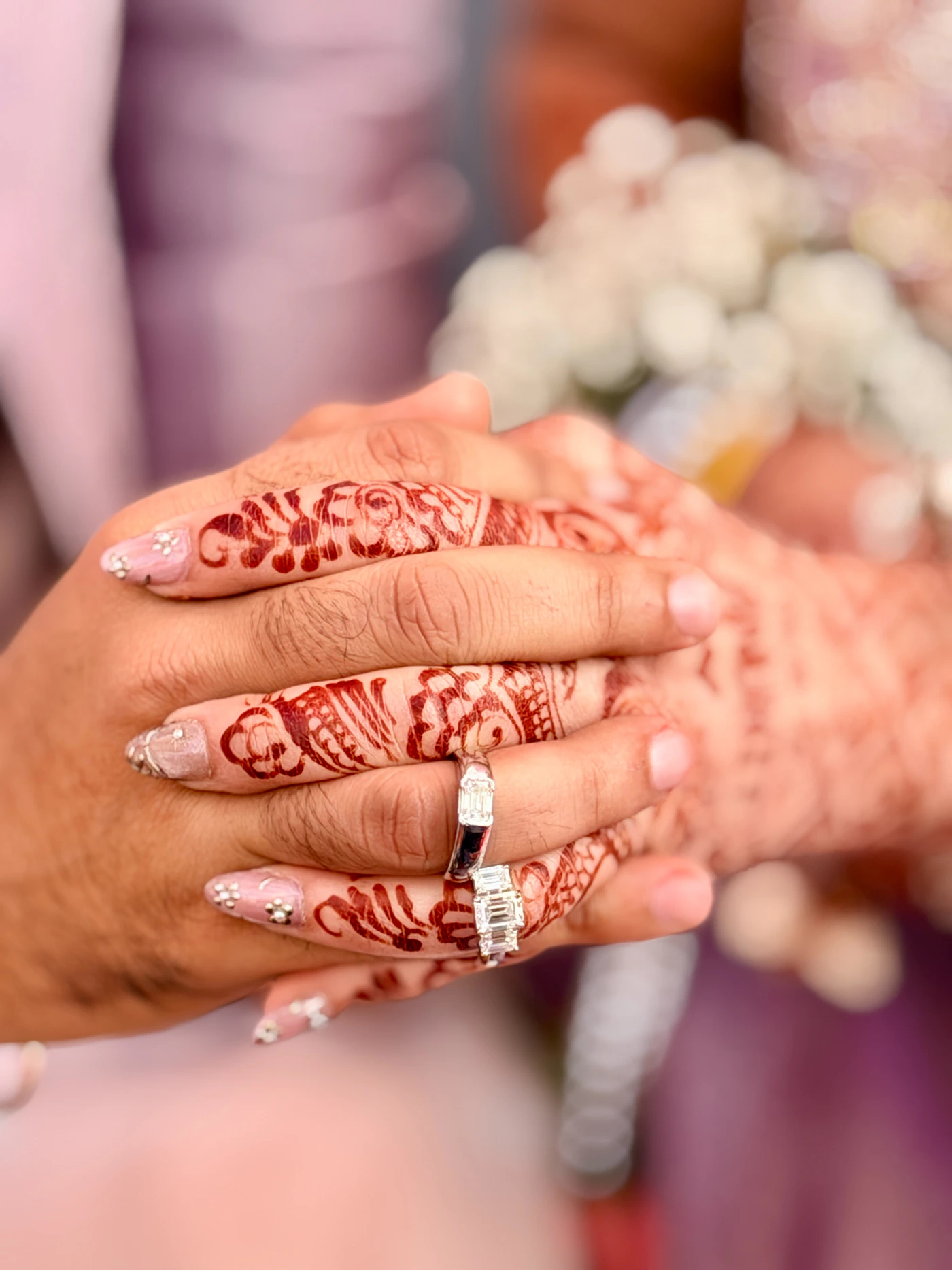 Bride and groom holding hands with intricate Mehendi and wedding rings