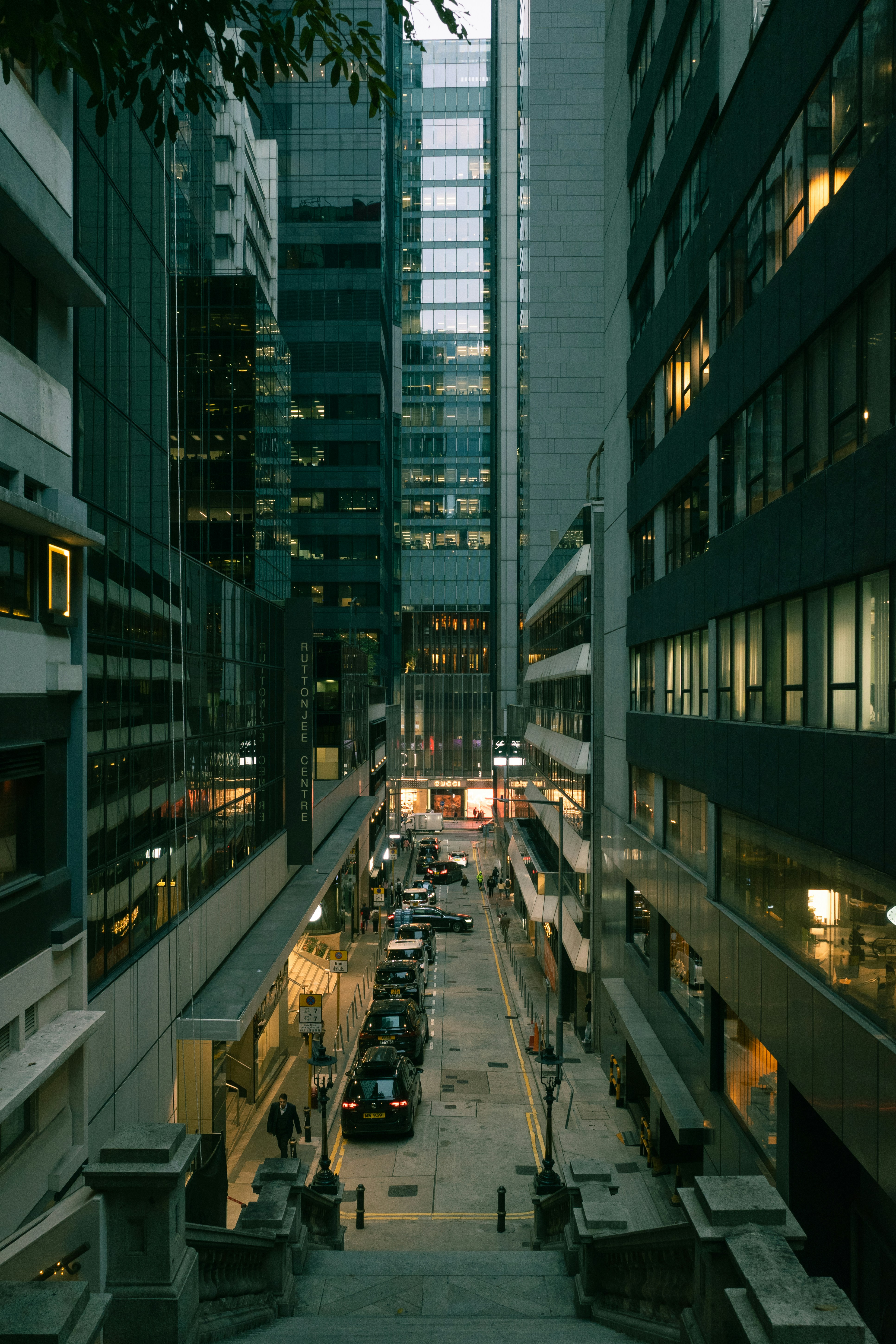 Tall buildings line a narrow city street with parked cars.