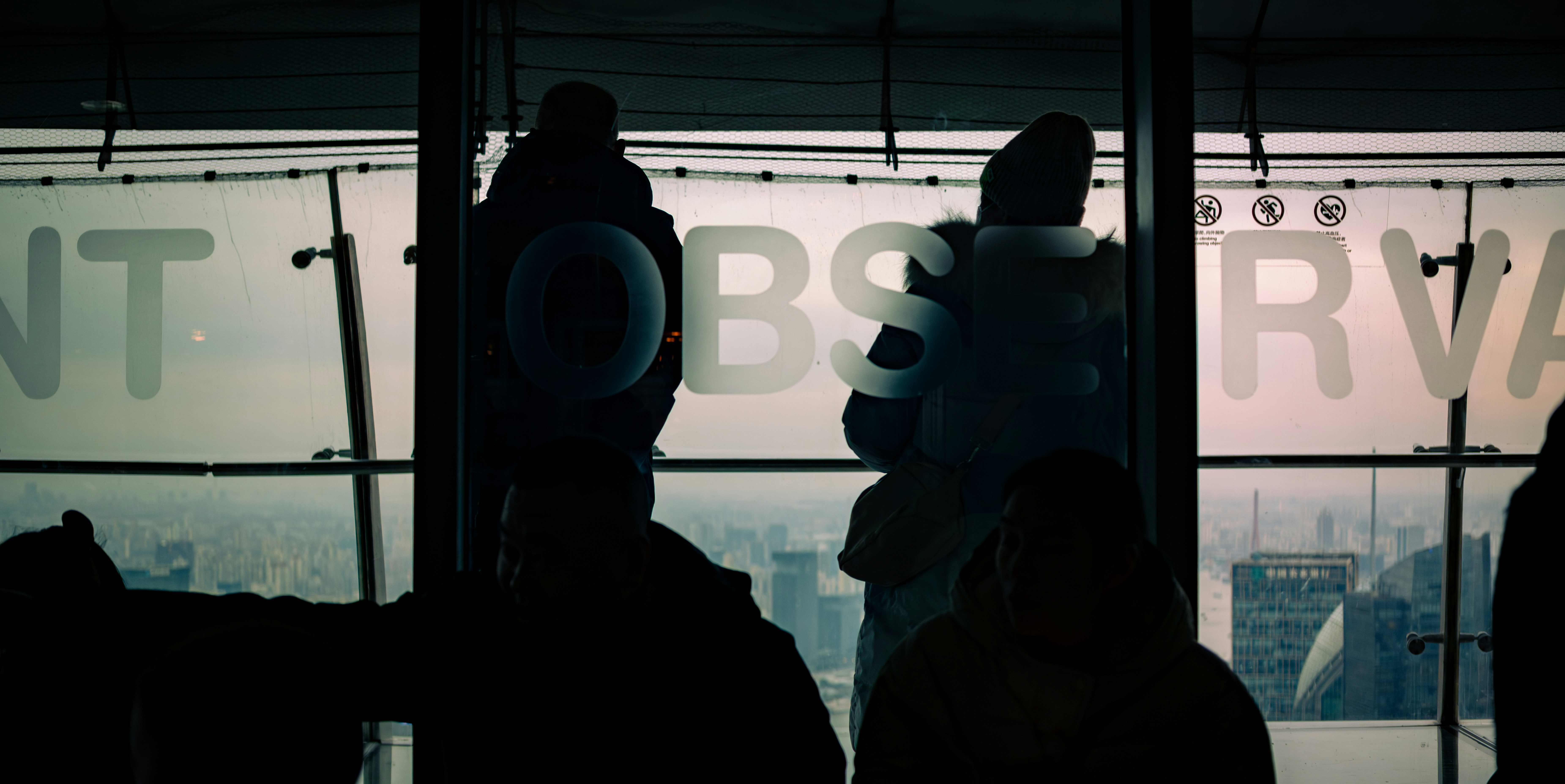 Silhouetted figures stand before a window with text.