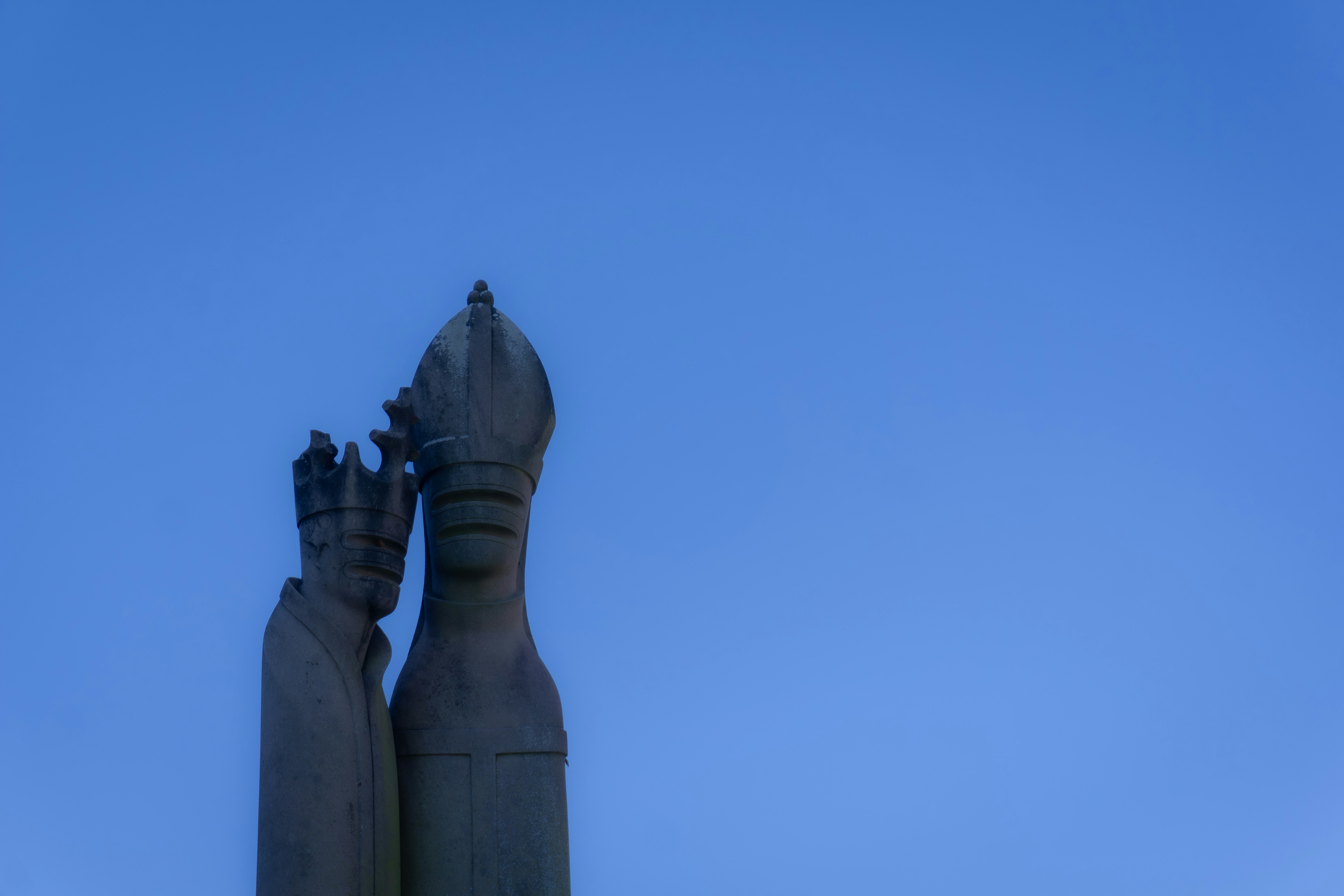 Statue of a person wearing a mitre against blue sky