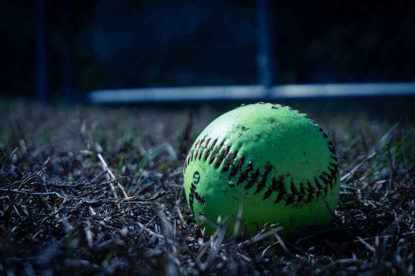 A neon green softball rests on dry grass