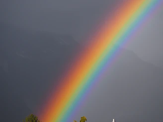 A vibrant rainbow arcs across a dark, stormy sky.