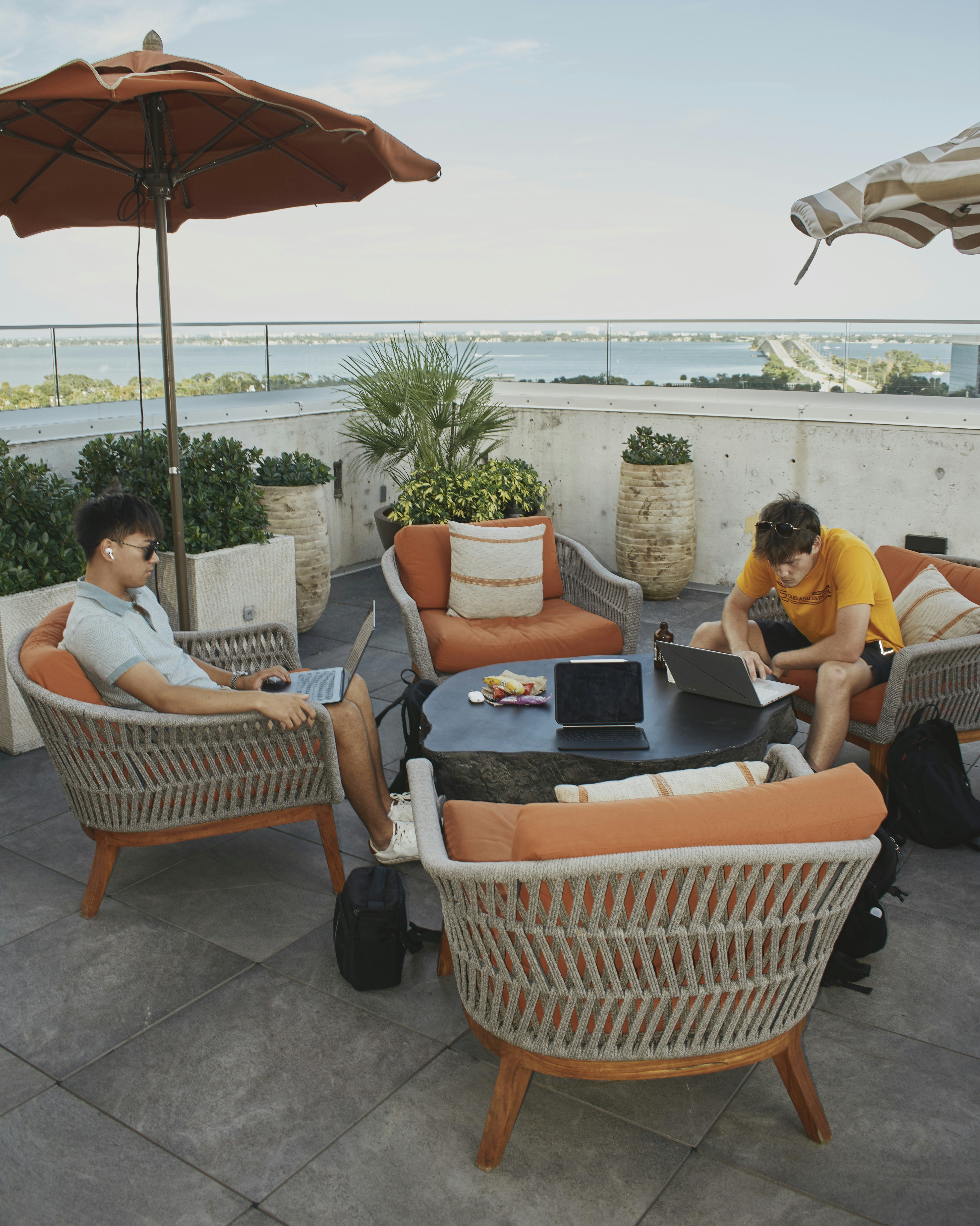 Two men working on laptops on a rooftop patio.