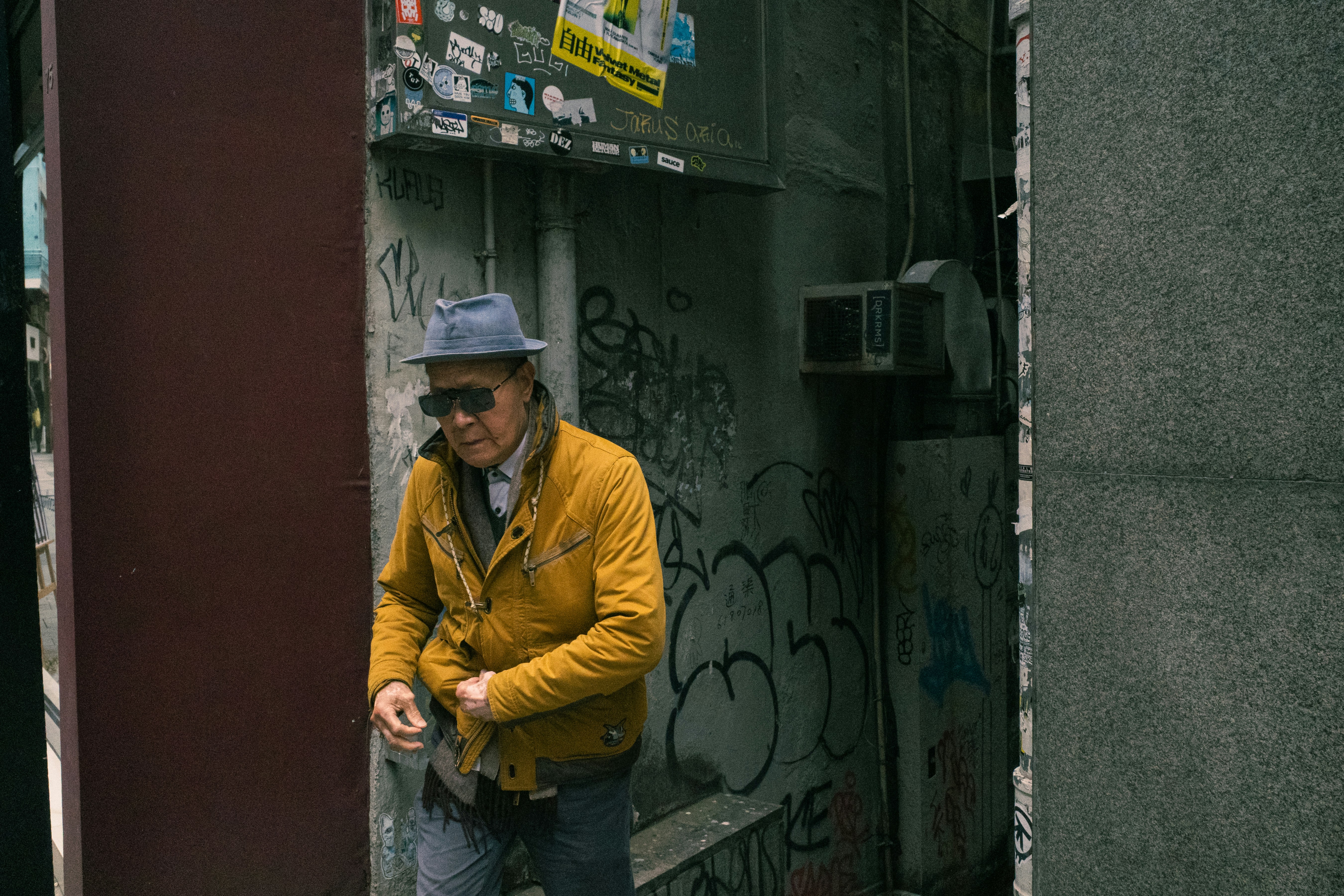 Man in yellow jacket and hat walks down alley.