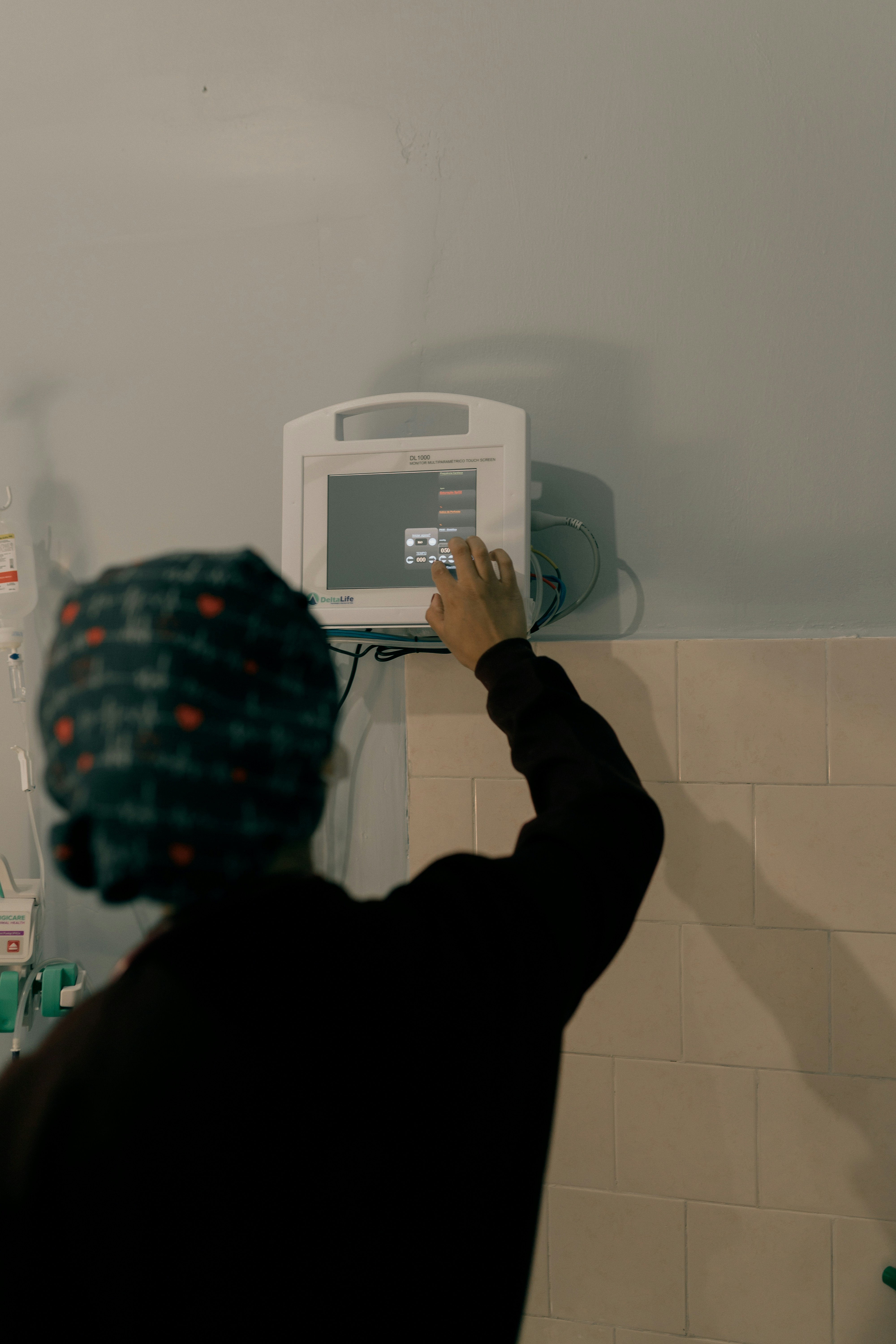 A person adjusts a medical monitor in a tiled room.