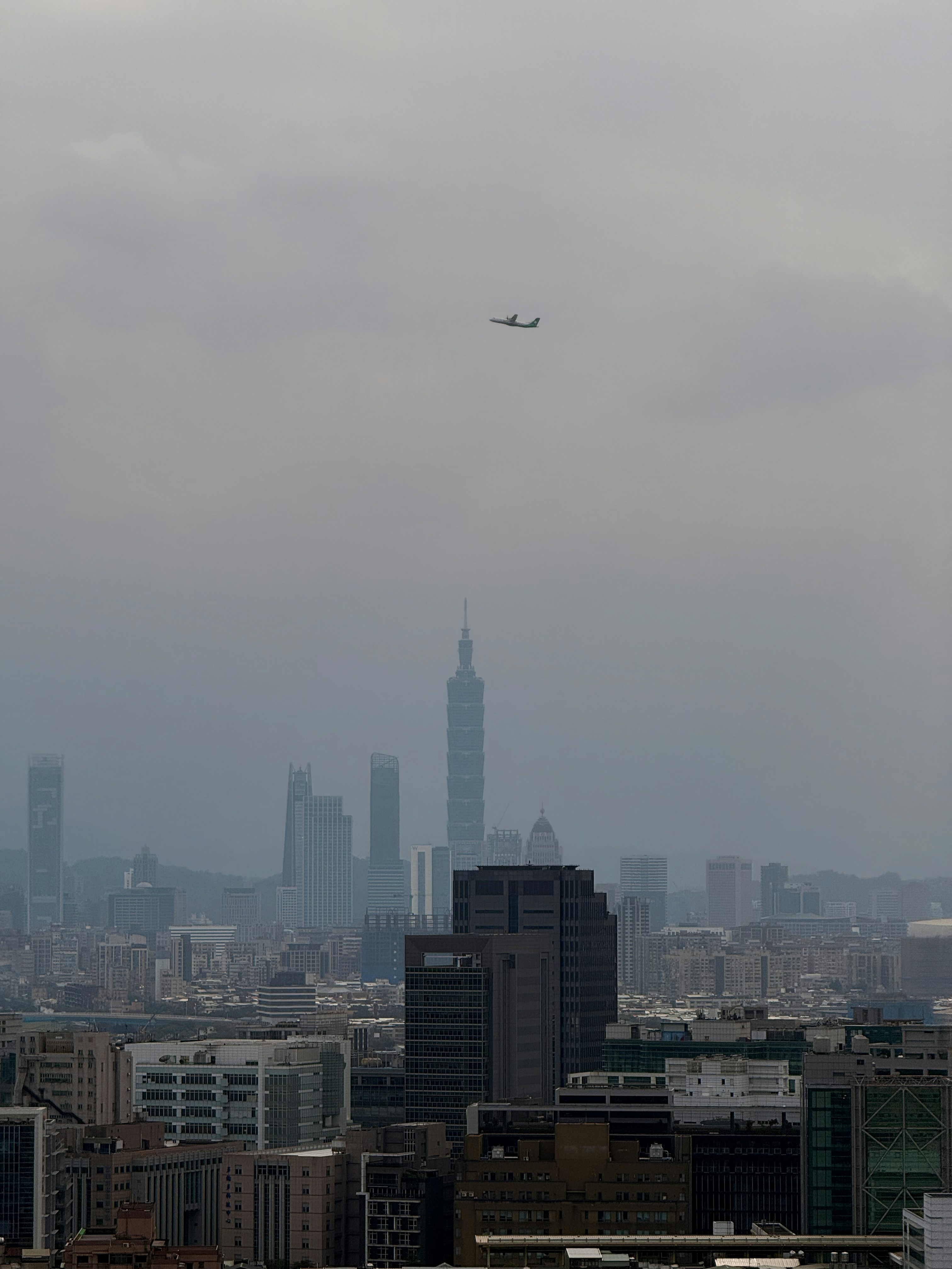 Airplane flying over a hazy cityscape with tall buildings.