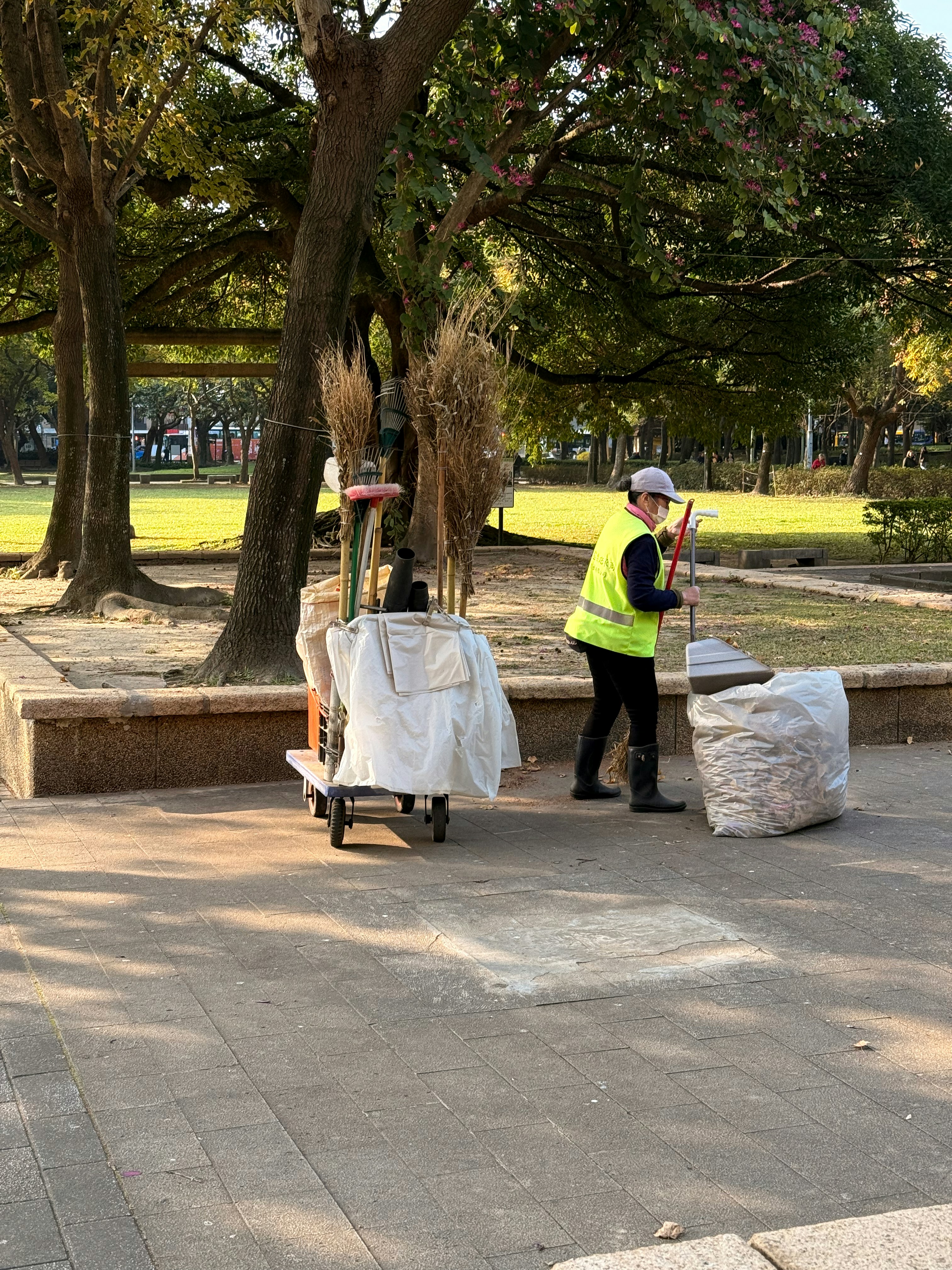 A person sweeps leaves in a park with a cart.