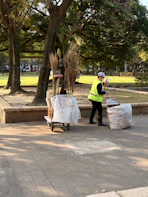 A person sweeps leaves in a park with a cart.