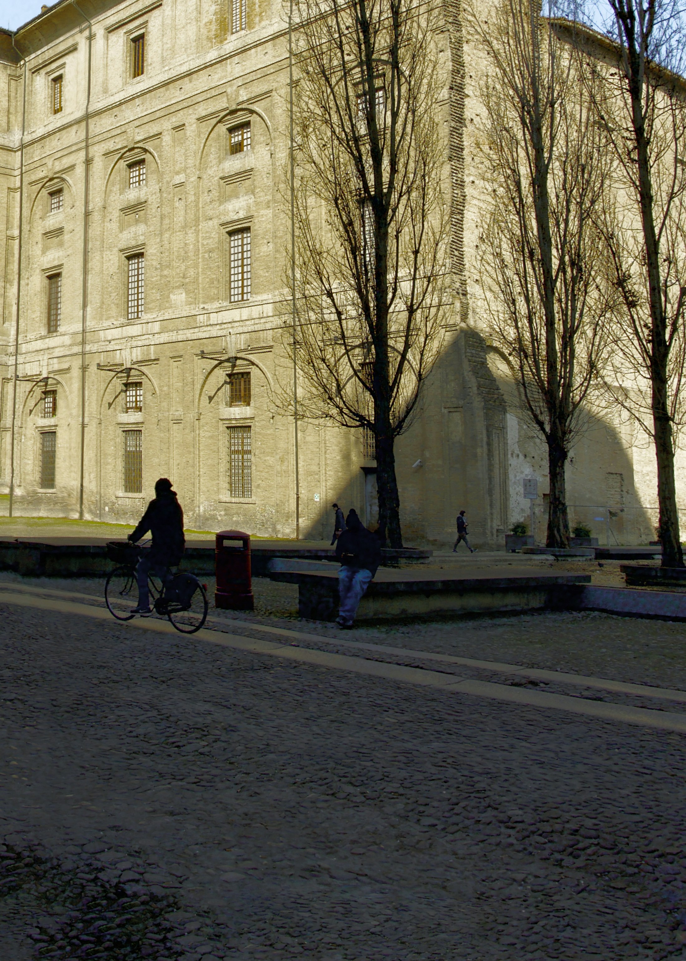 People cycling and sitting near a large building.