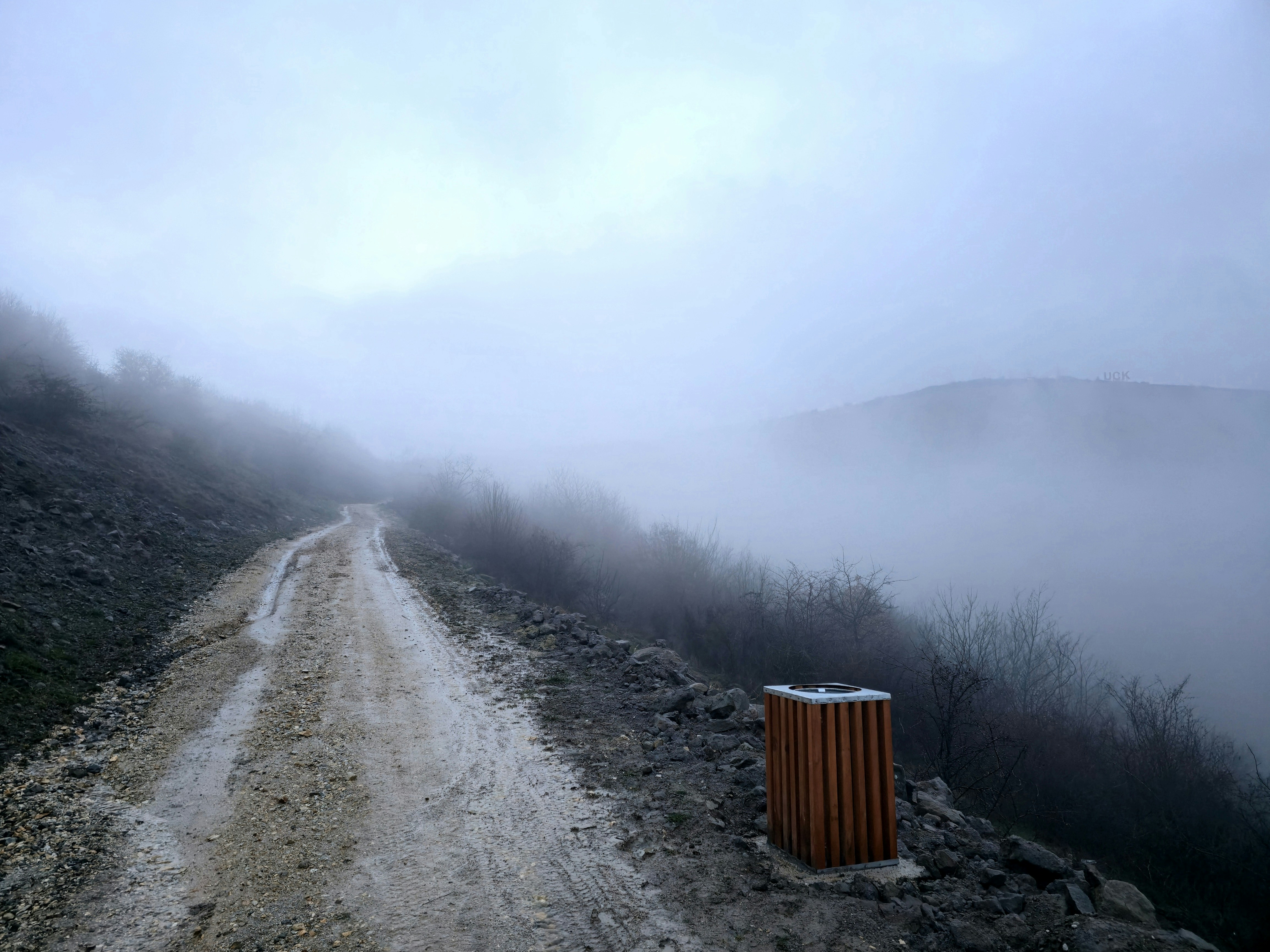 A dirt road winds through a foggy, mountainous landscape.