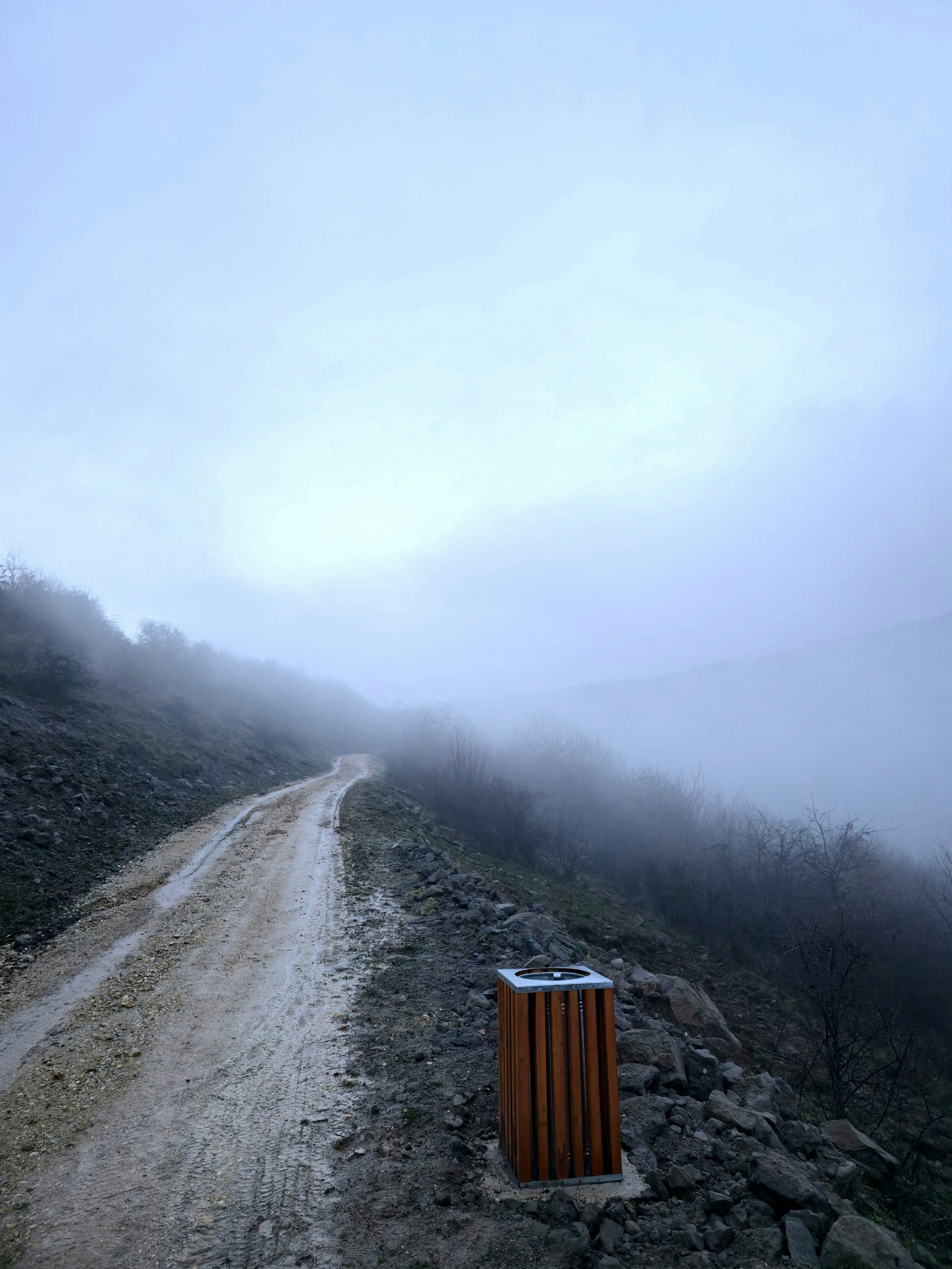 A dirt road winds through a foggy, mountainous landscape.