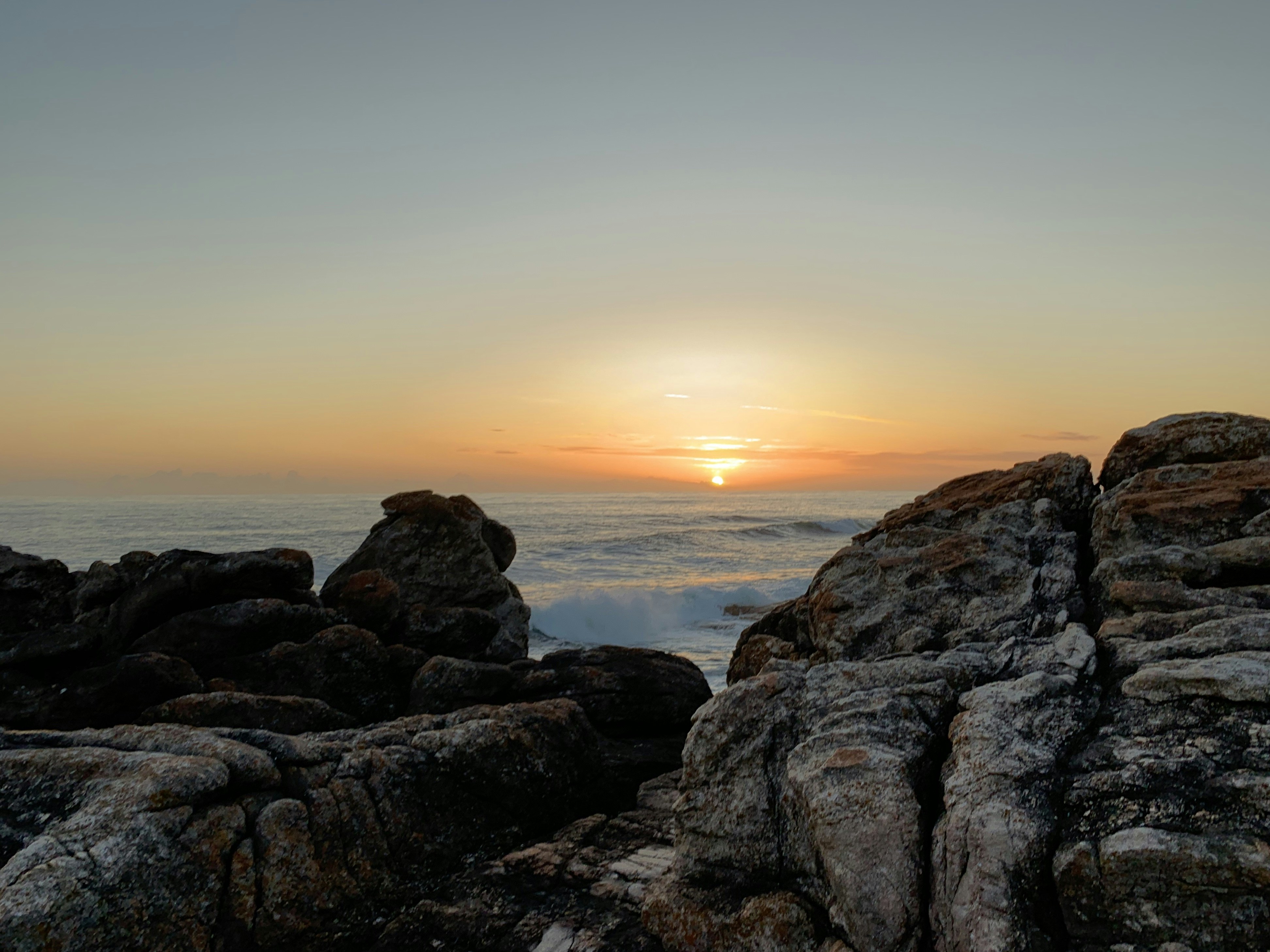 Sunrise over the ocean viewed through rocky foreground.