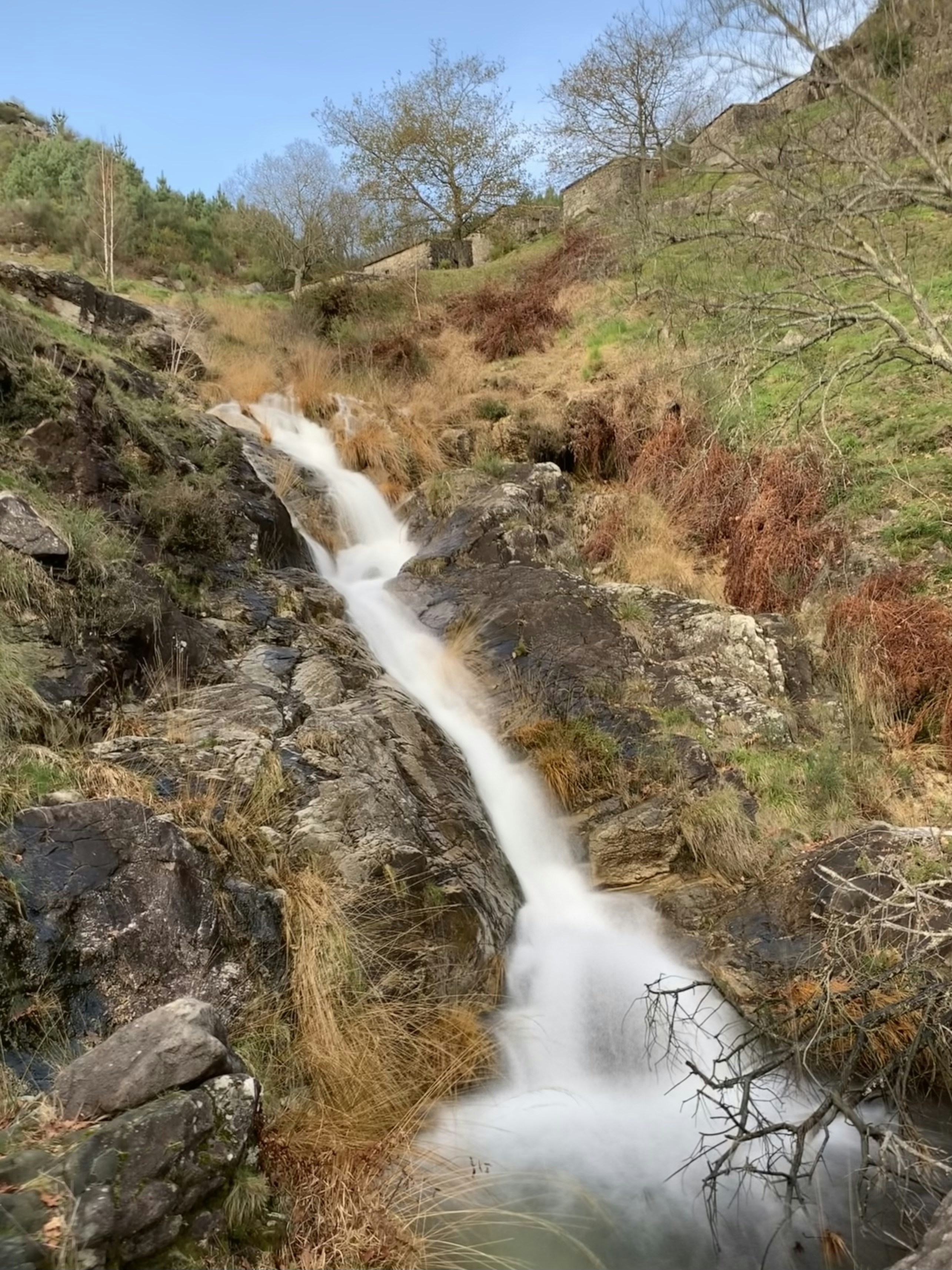 A waterfall cascades down a rocky hillside with dry grass.