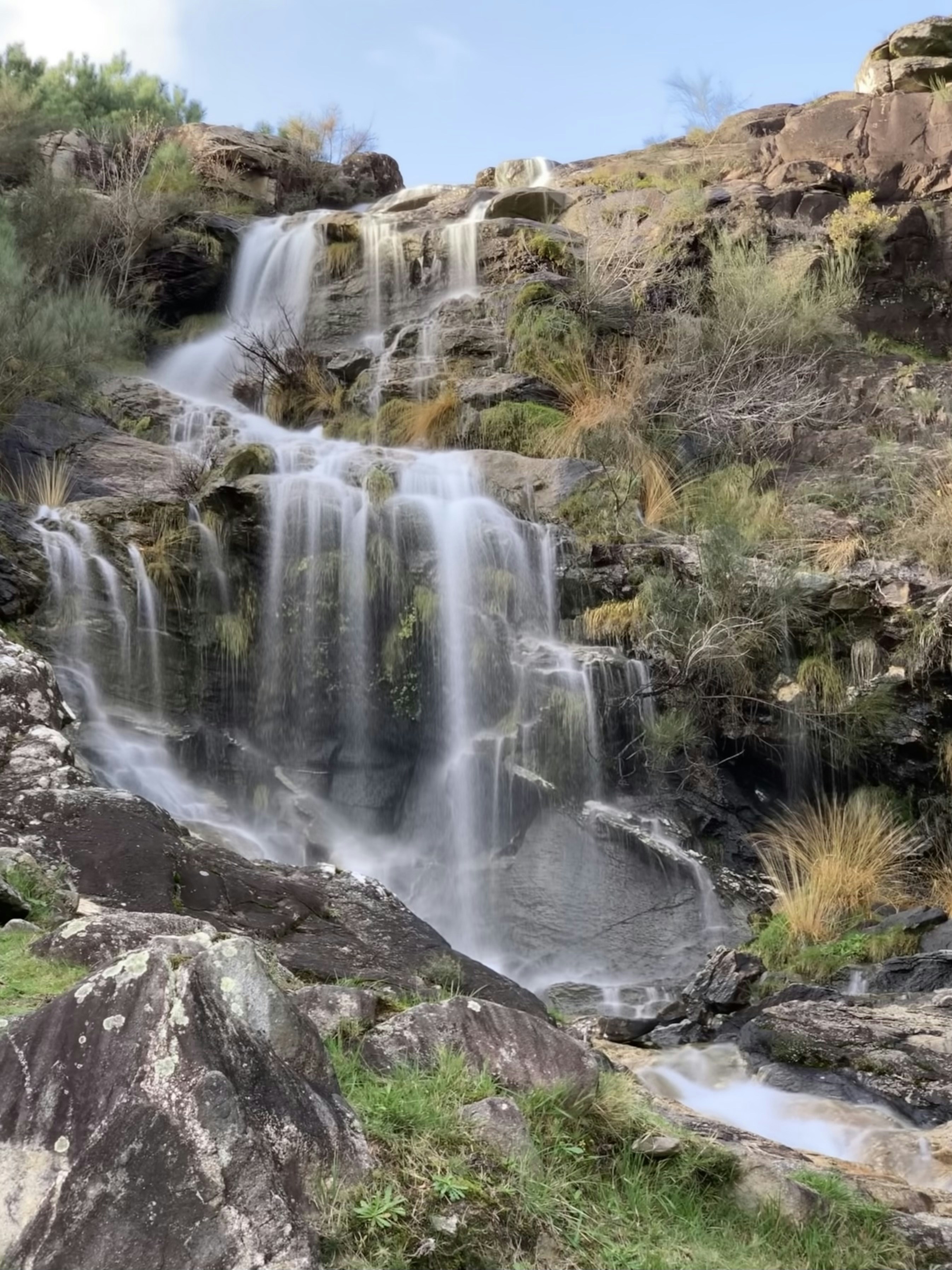 A cascading waterfall flows down a rocky, overgrown hillside.