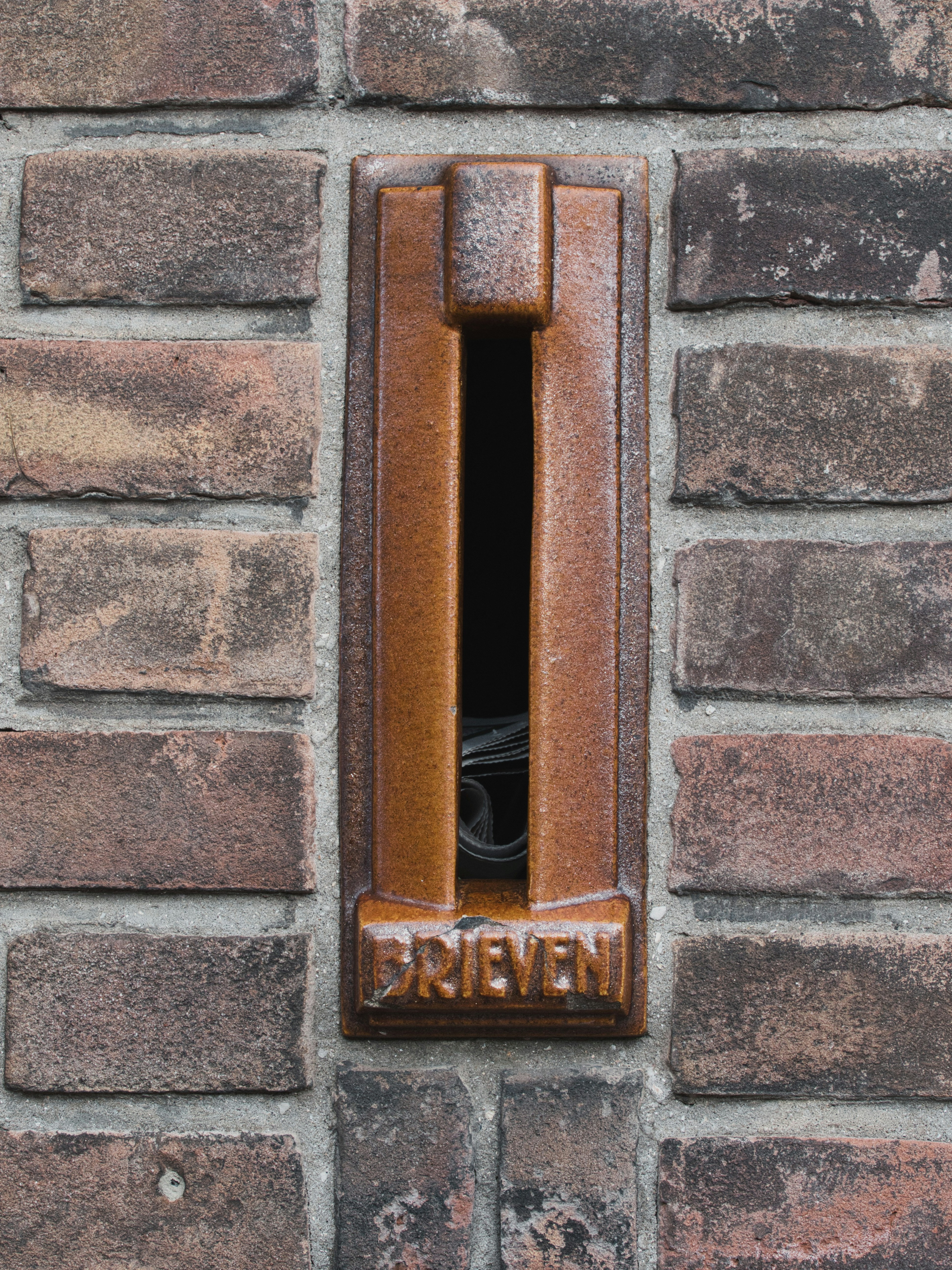 A vintage mail slot on a brick wall.