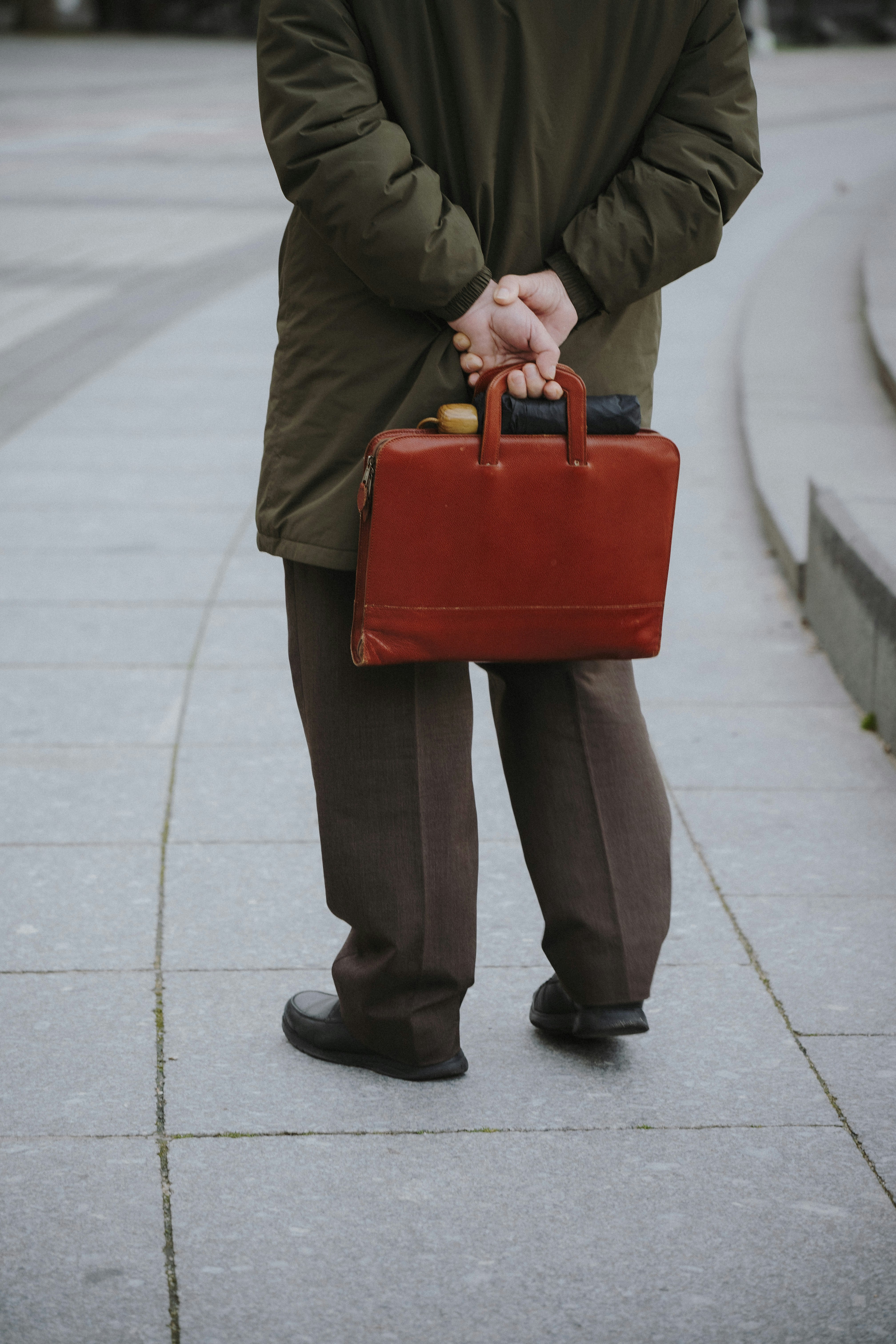 Uomo in cappotto che tiene una valigetta marrone dietro la schiena