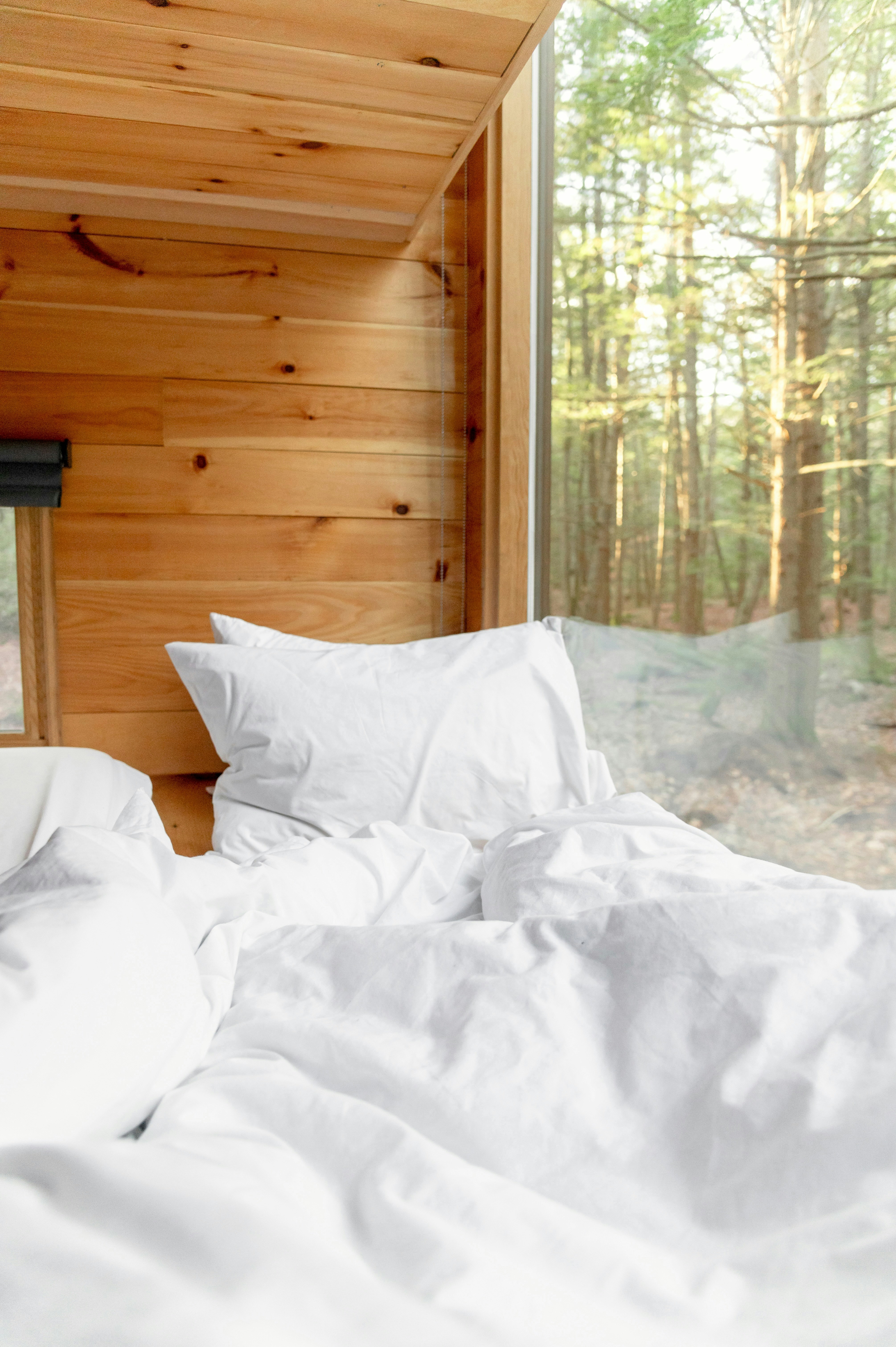Cama aconchegante com lençóis brancos ao lado da janela da floresta.