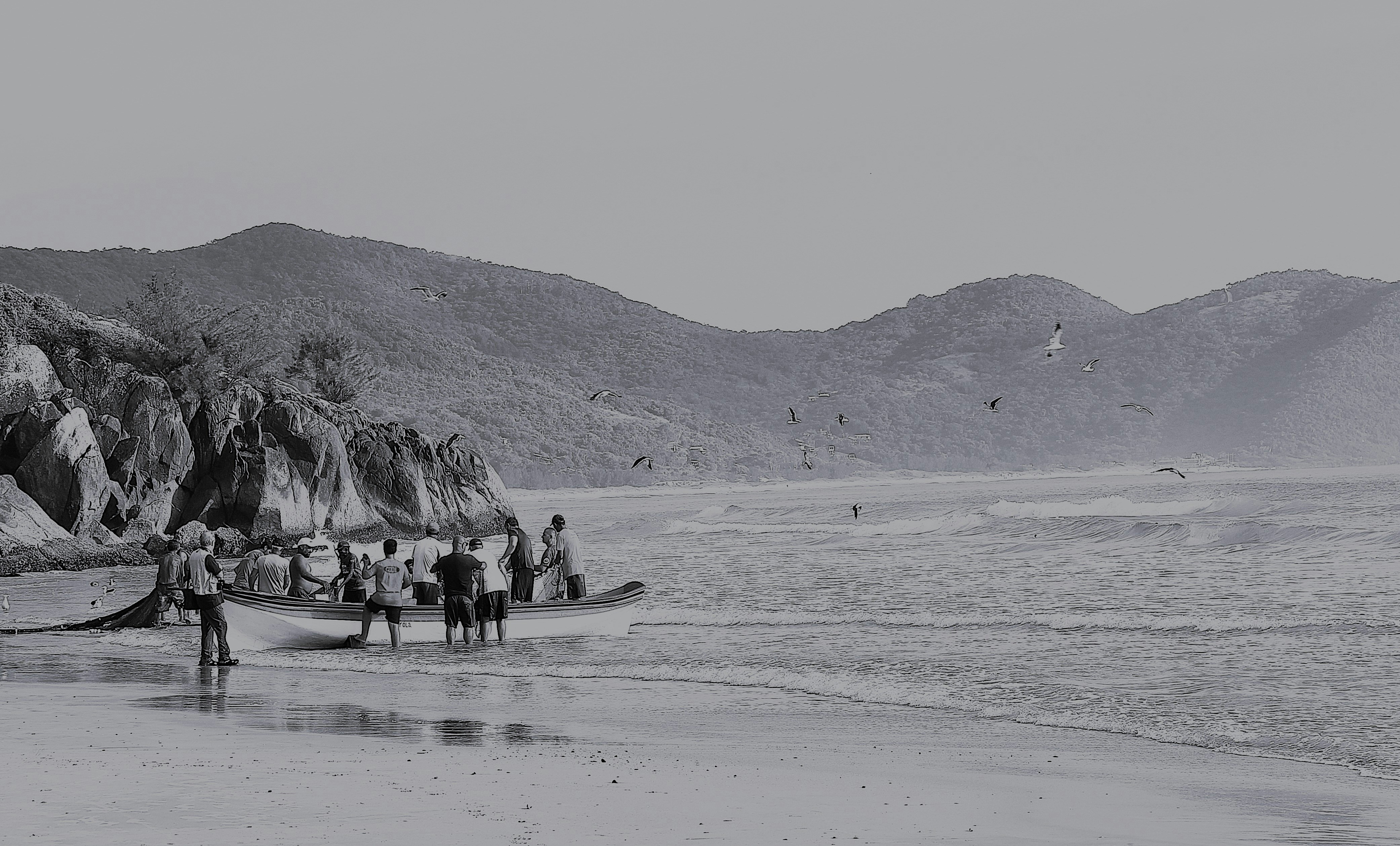 People gather on a sandy beach with rolling hills behind.