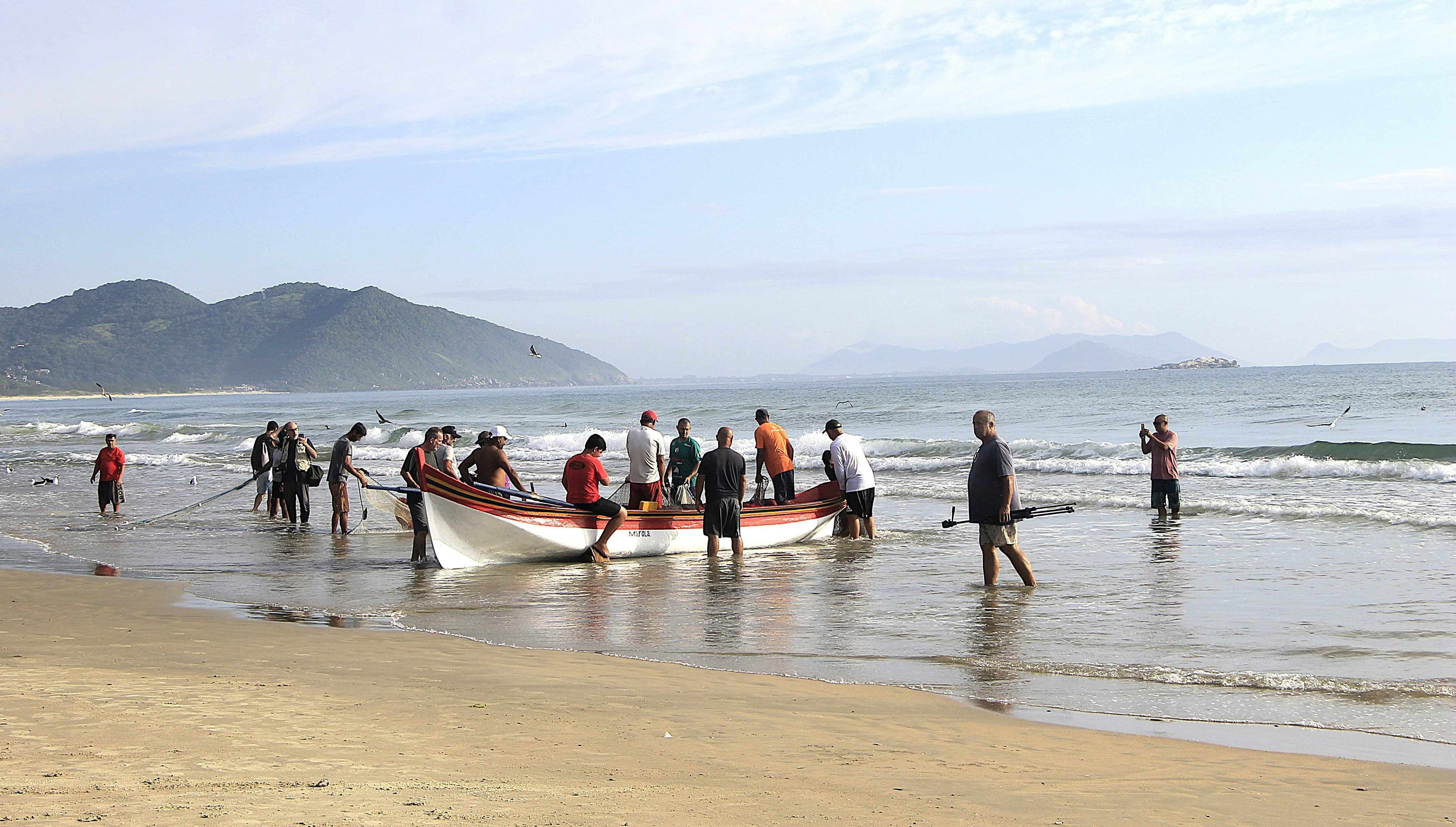 Fishermen pulling a boat ashore on a sandy beach.