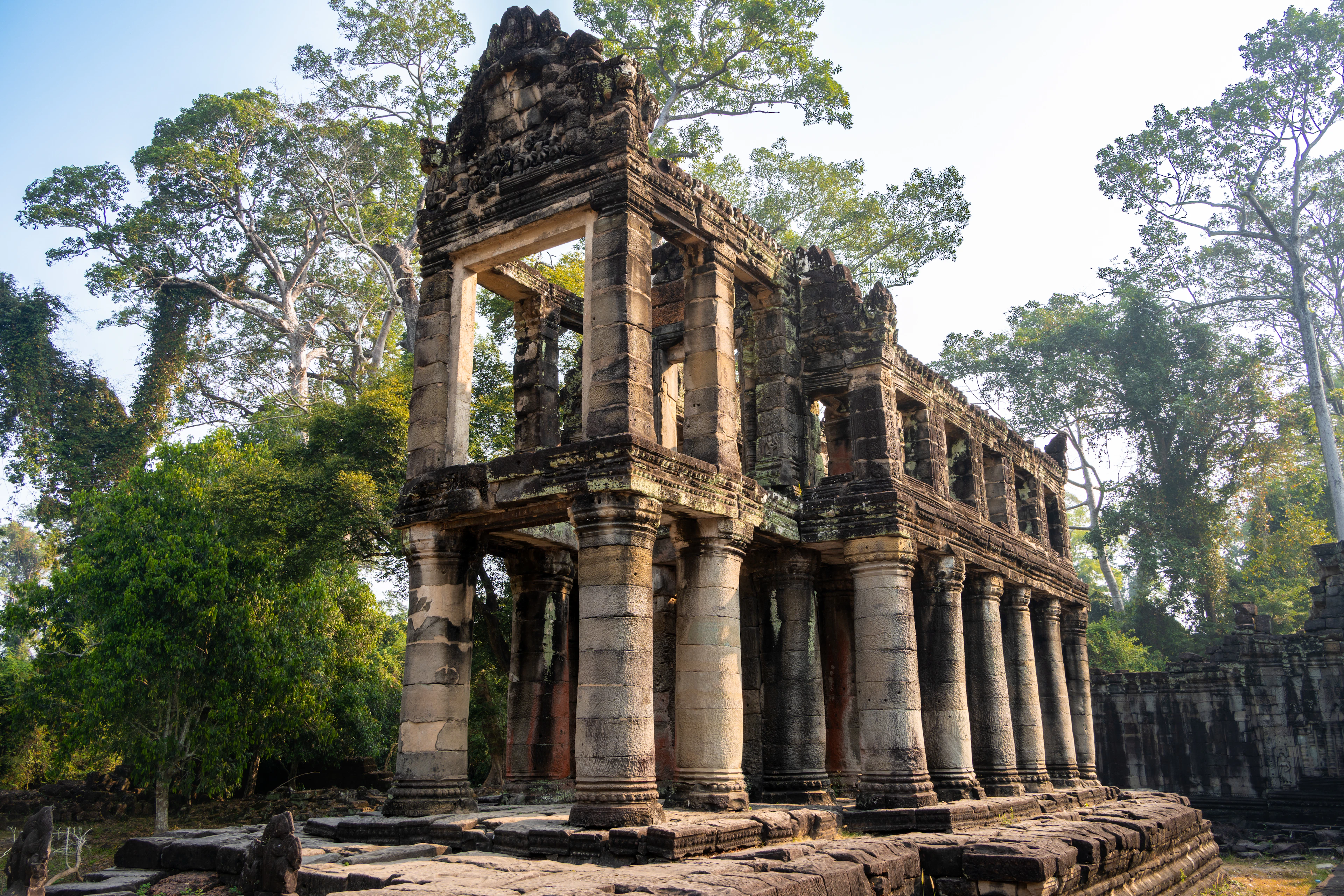 The two-storey pillared pavilion at Preah Khan, its rare round stone columns standing in low morning sun against the surrounding jungle canopy