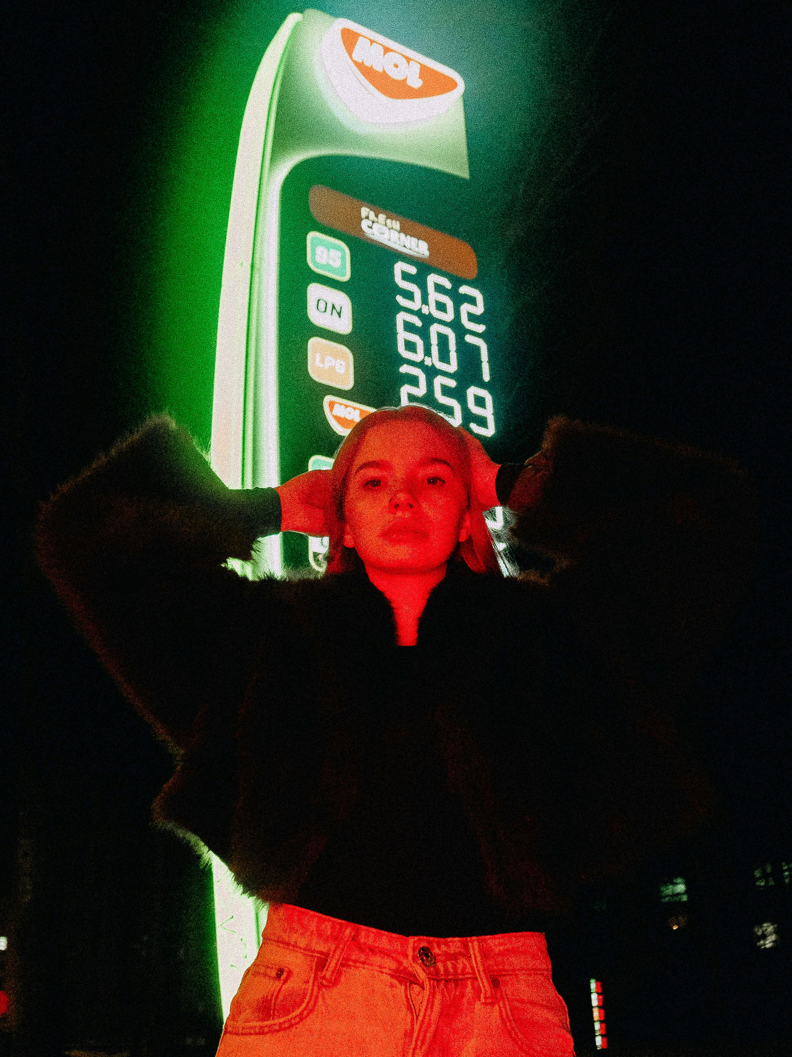 Woman posing by a gas station sign at night