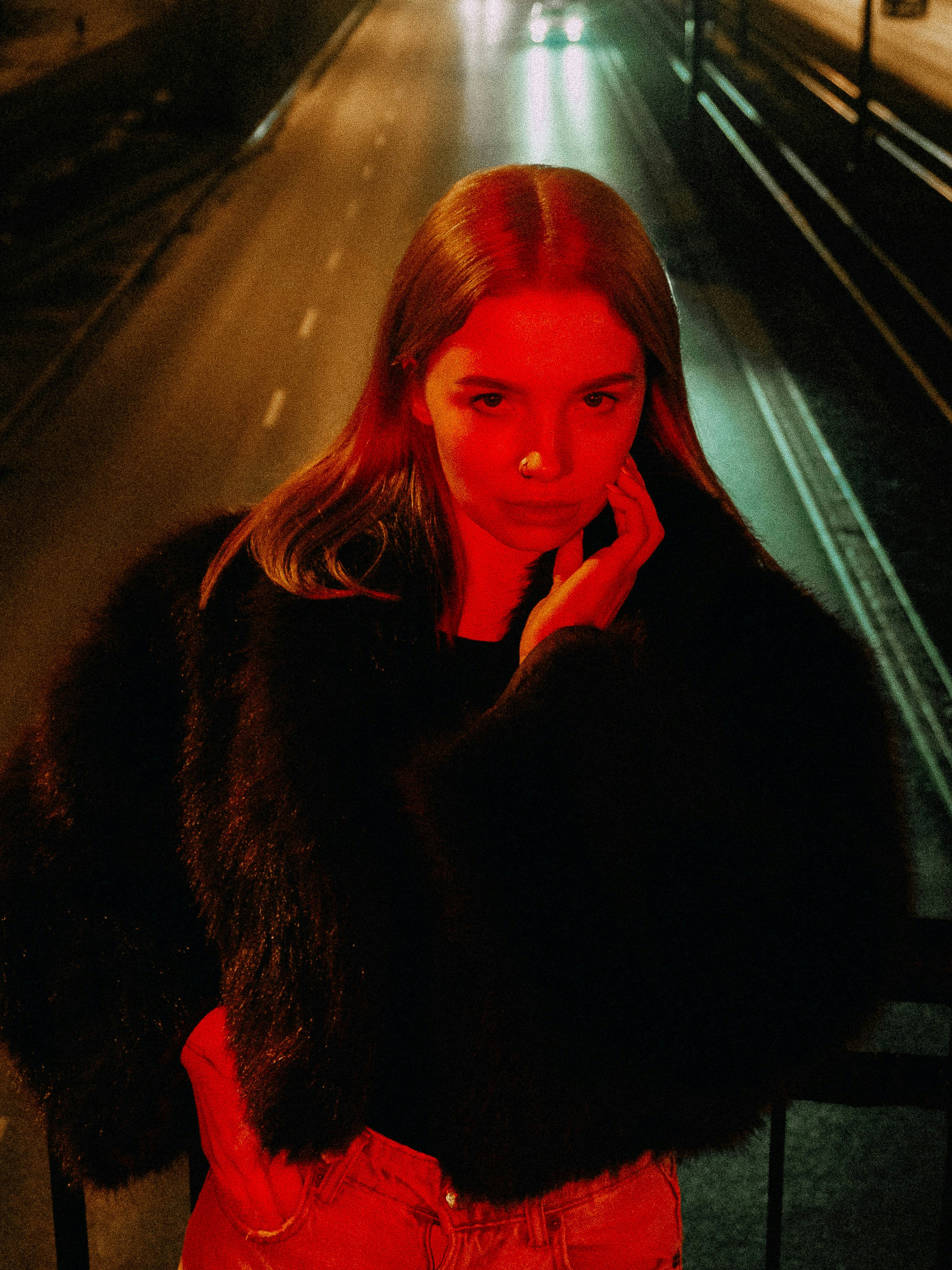 Young woman in fur coat under red light at night