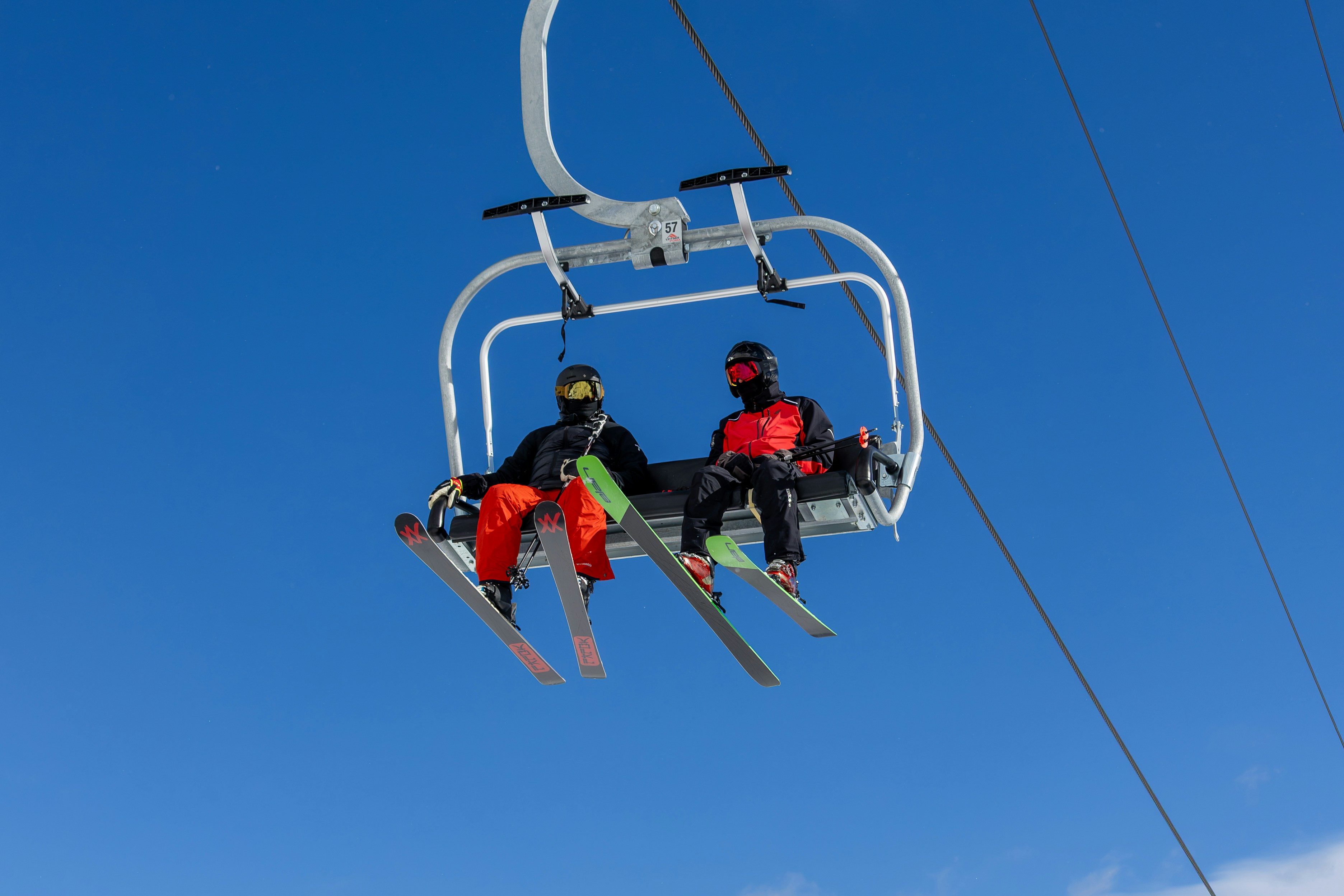 Two skiers ride a chairlift against a blue sky