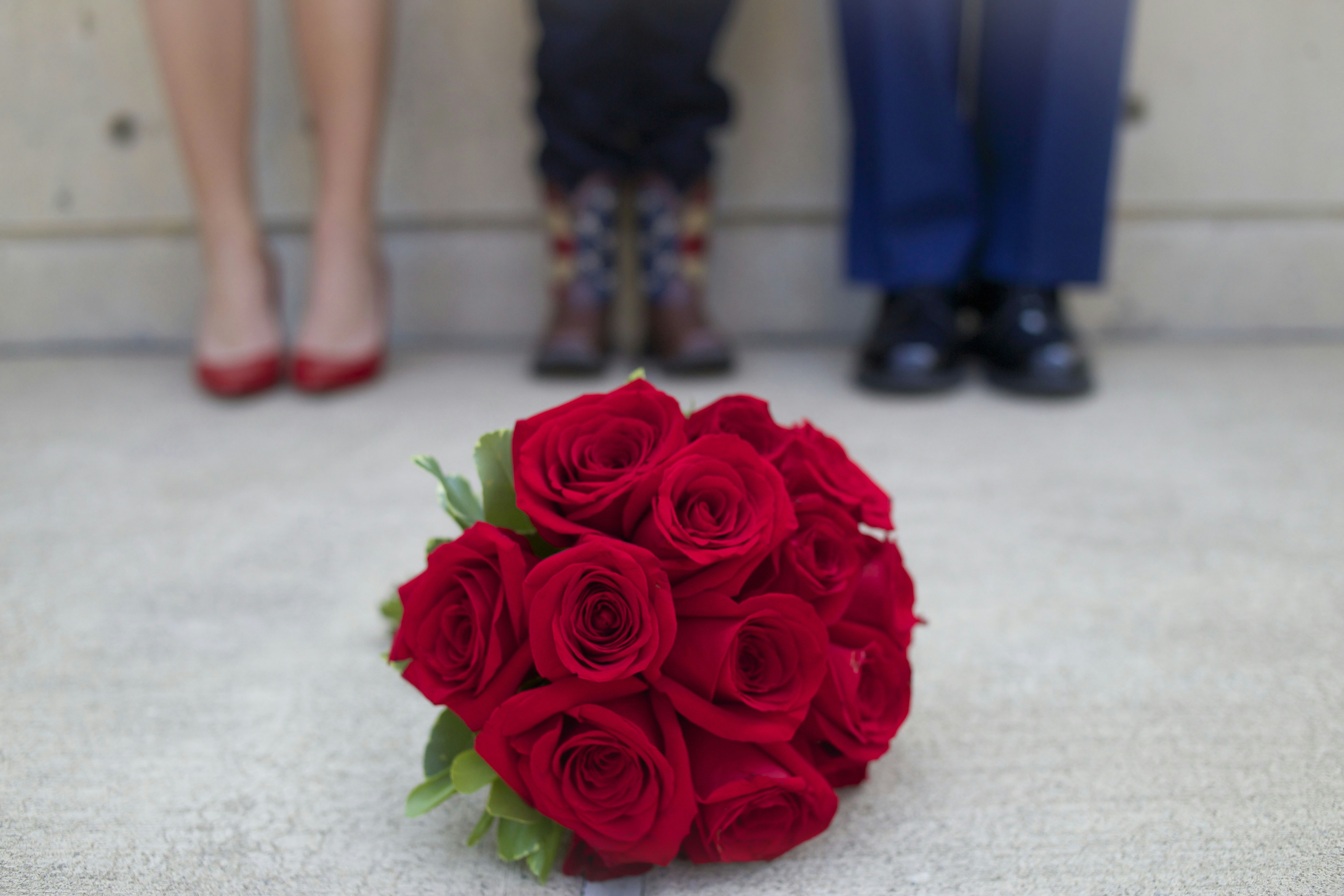 A bouquet of red roses rests before three people.