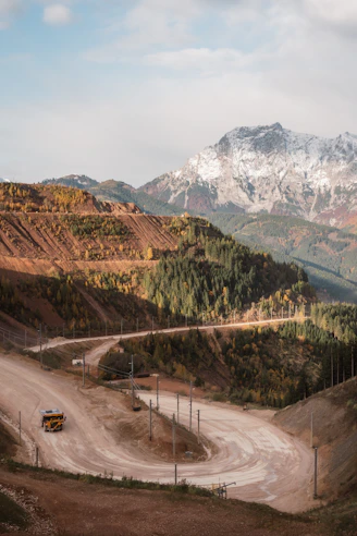A winding dirt road leads through autumn mountains.