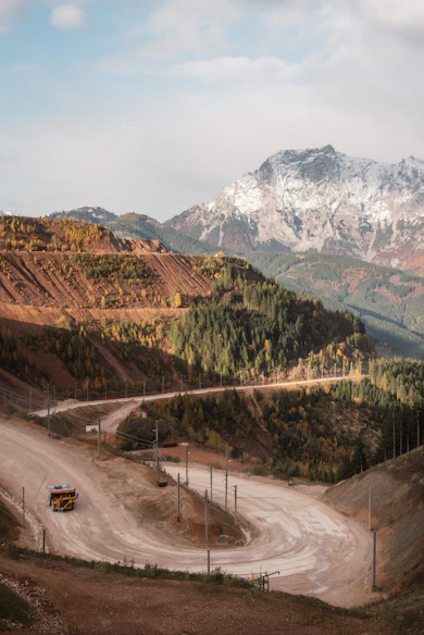 A winding dirt road leads through autumn mountains.
