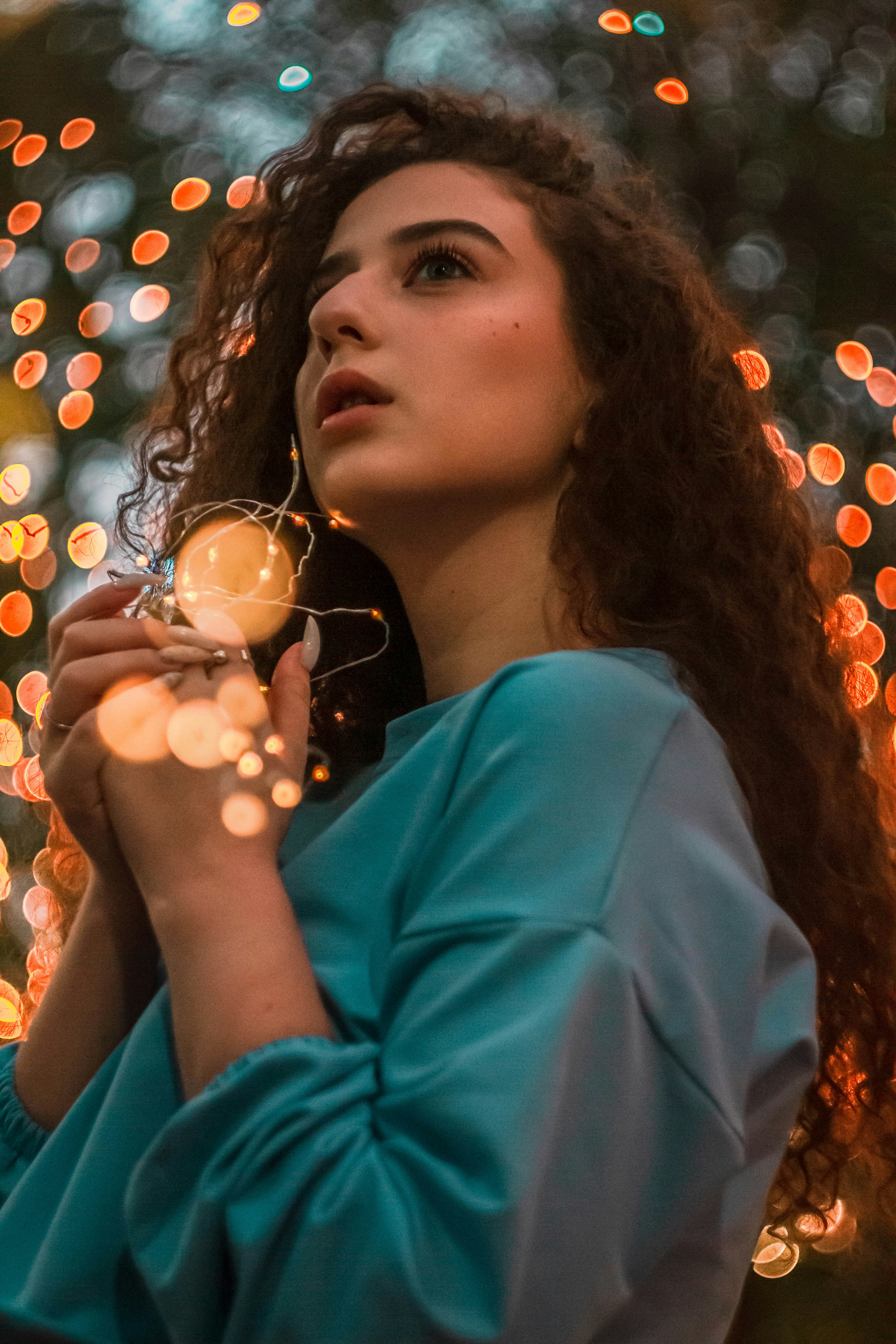 Wanita muda memegang lampu string yang menyala dengan latar belakang bokeh