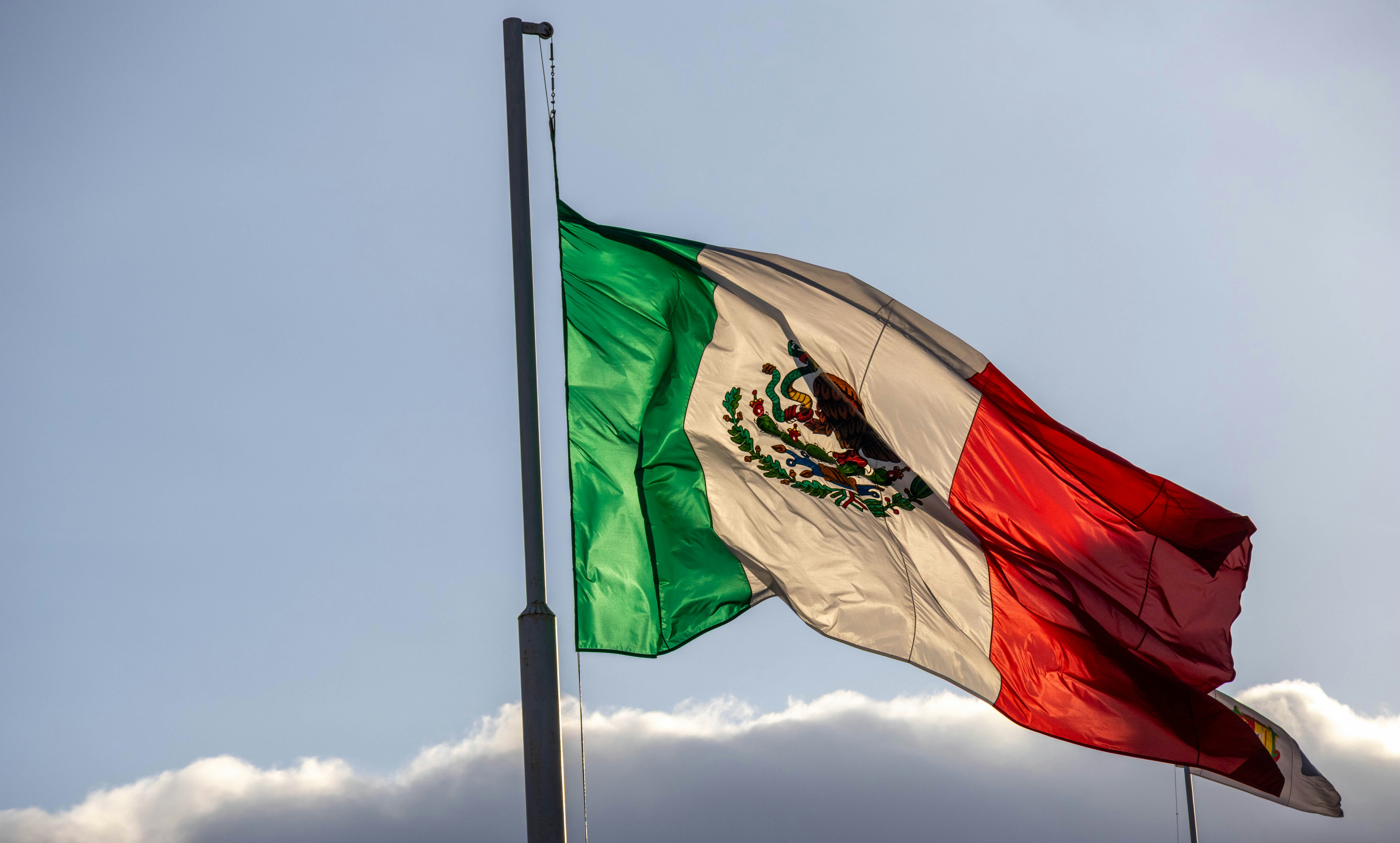 The mexican flag waves proudly against a blue sky.