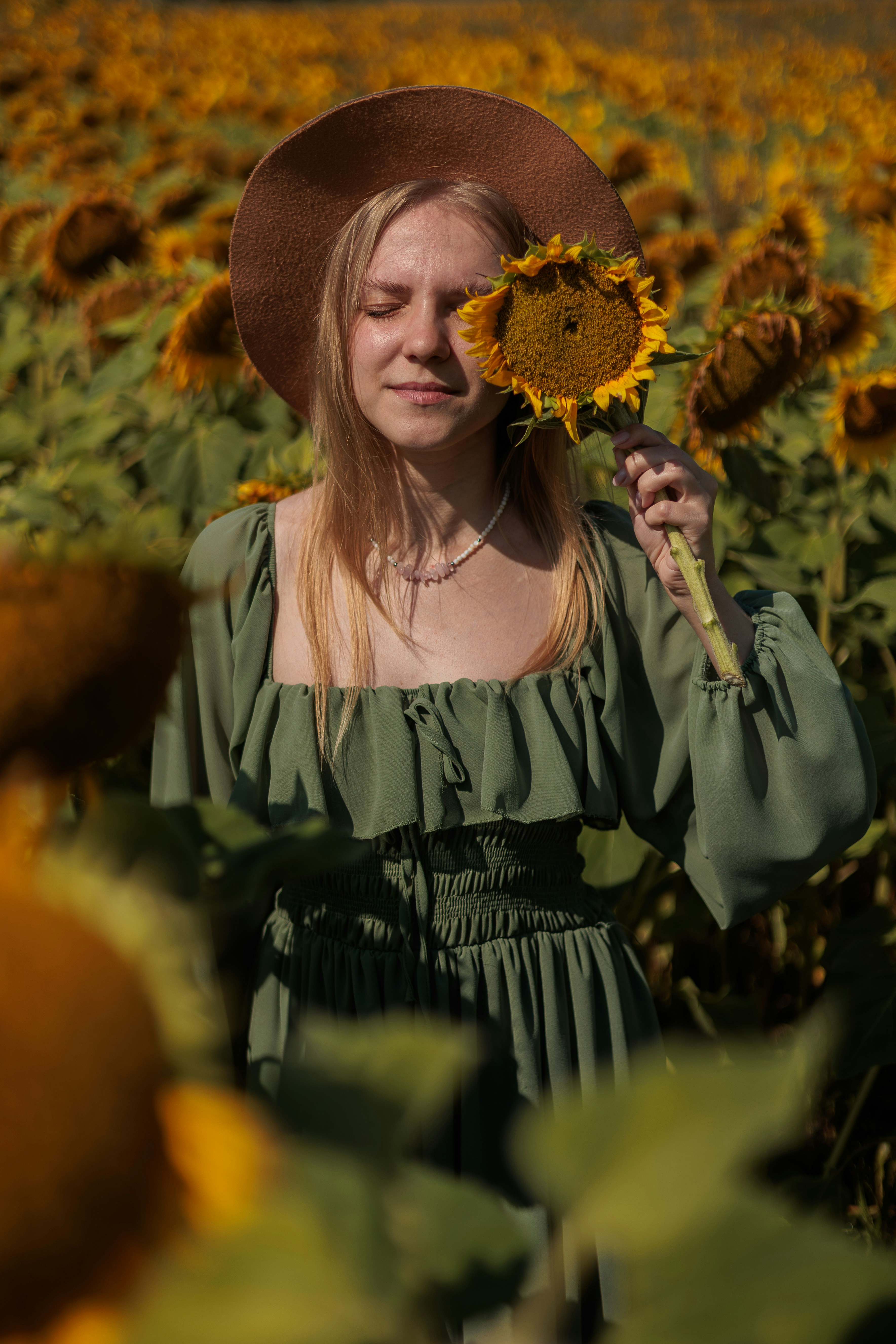 Frau mit Hut, die eine Sonnenblume auf einem Feld hält.