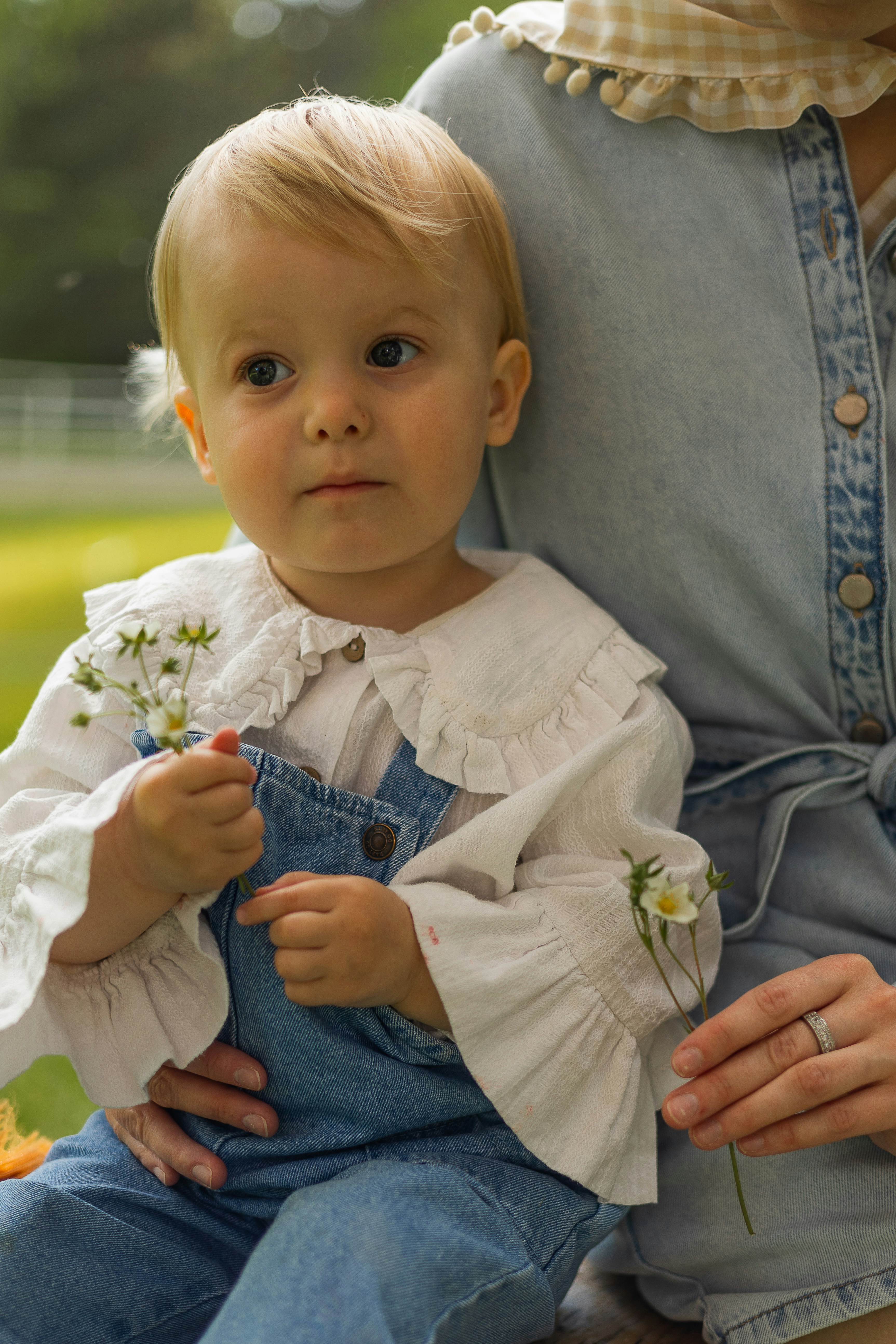 Ein kleines Kind im Overall-Kleidung hält Blumen draußen.