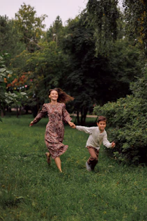 A woman and a boy running through a grassy park