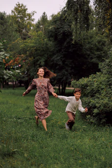 A woman and a boy running through a grassy park