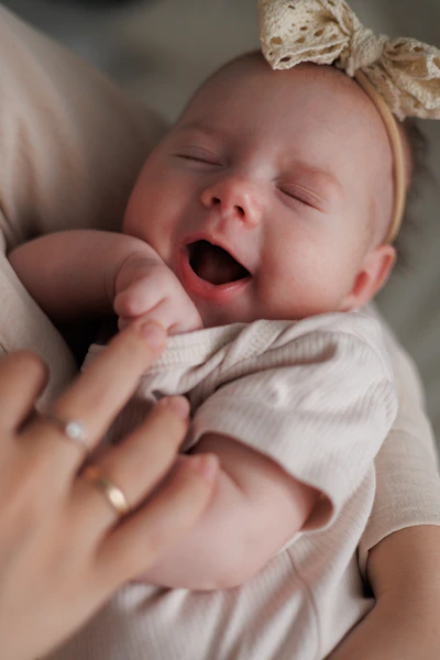 A yawning newborn baby with a bow on her head.