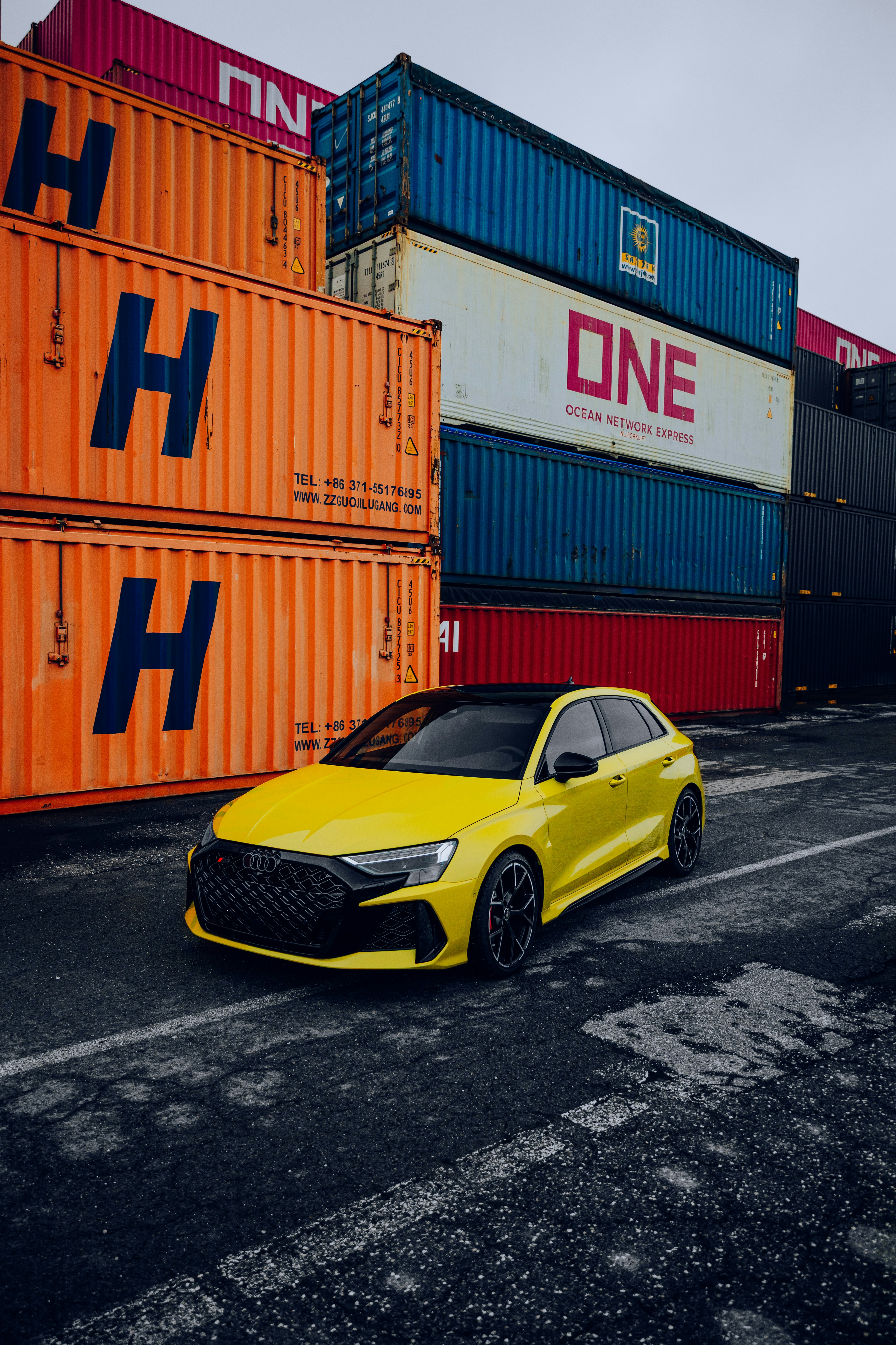 Yellow car parked near stacked shipping containers