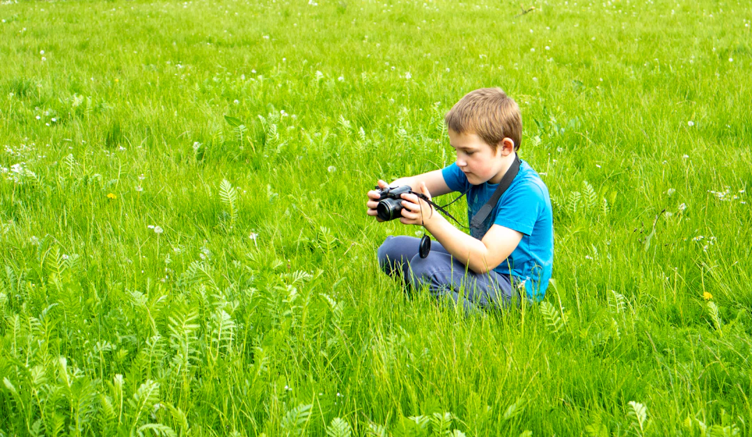 Young boy crouching in green grass with camera