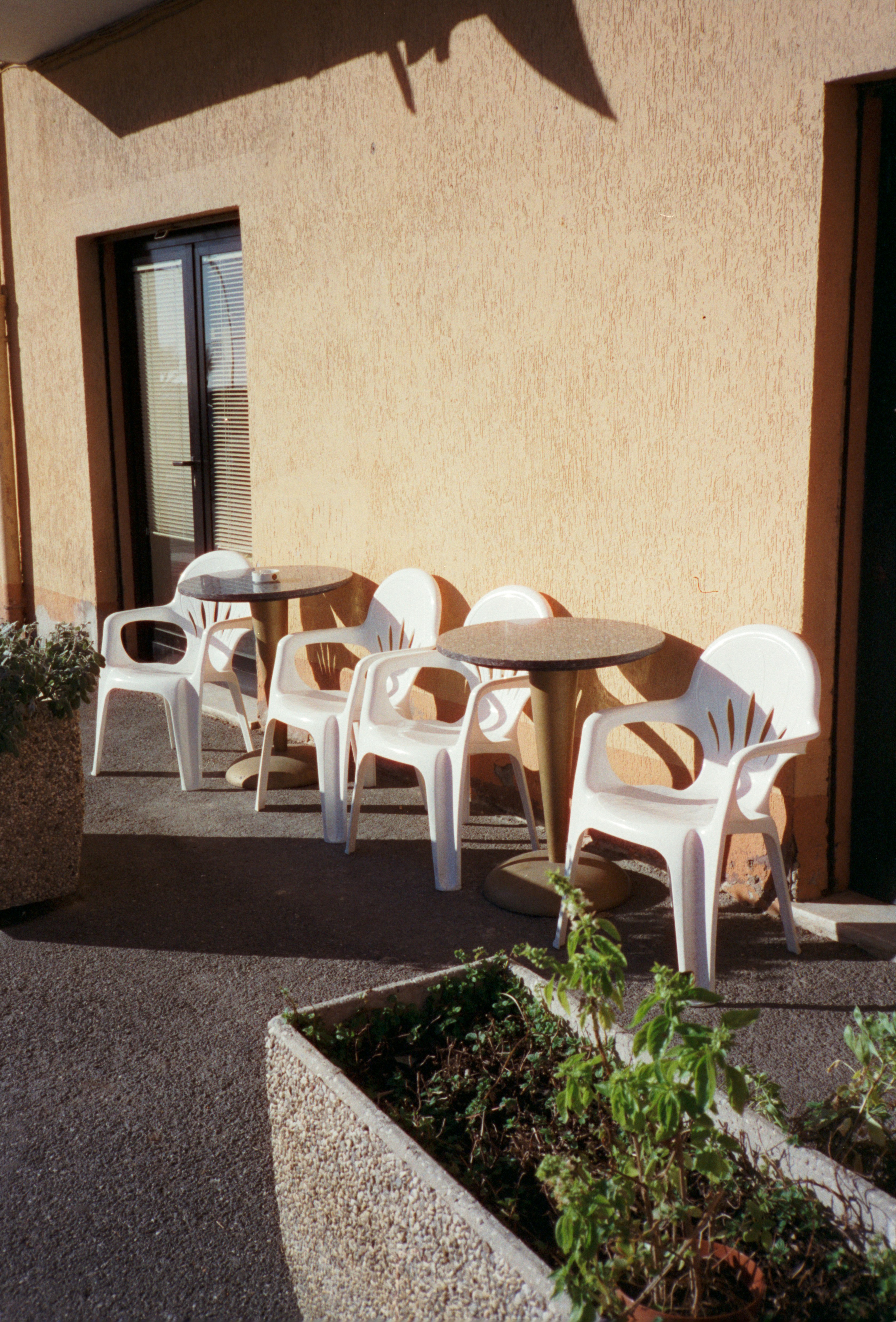 Weiße Stühle und Tische auf einer sonnigen Terrasse.