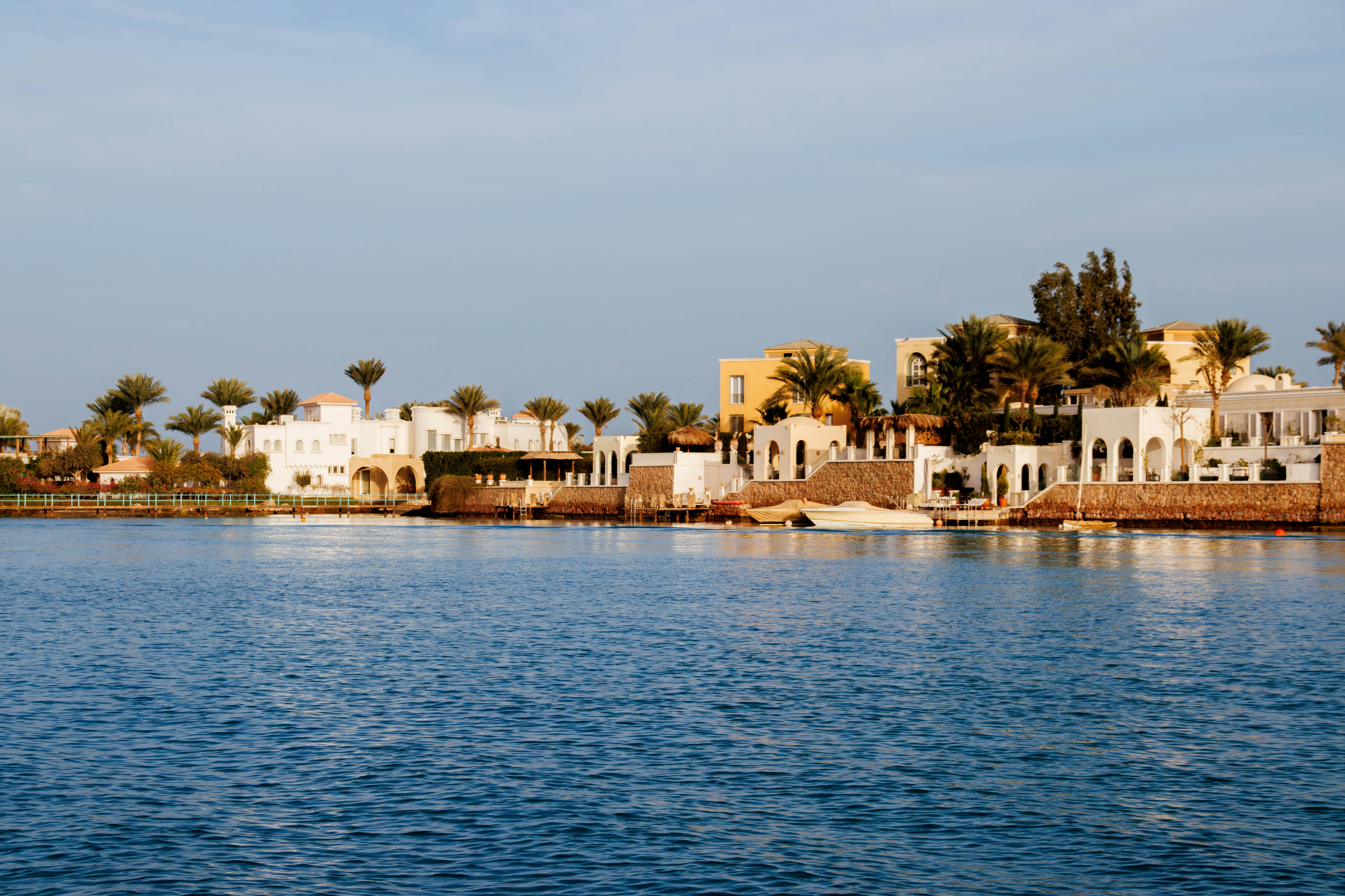 White buildings line a calm blue bay with palm trees.
