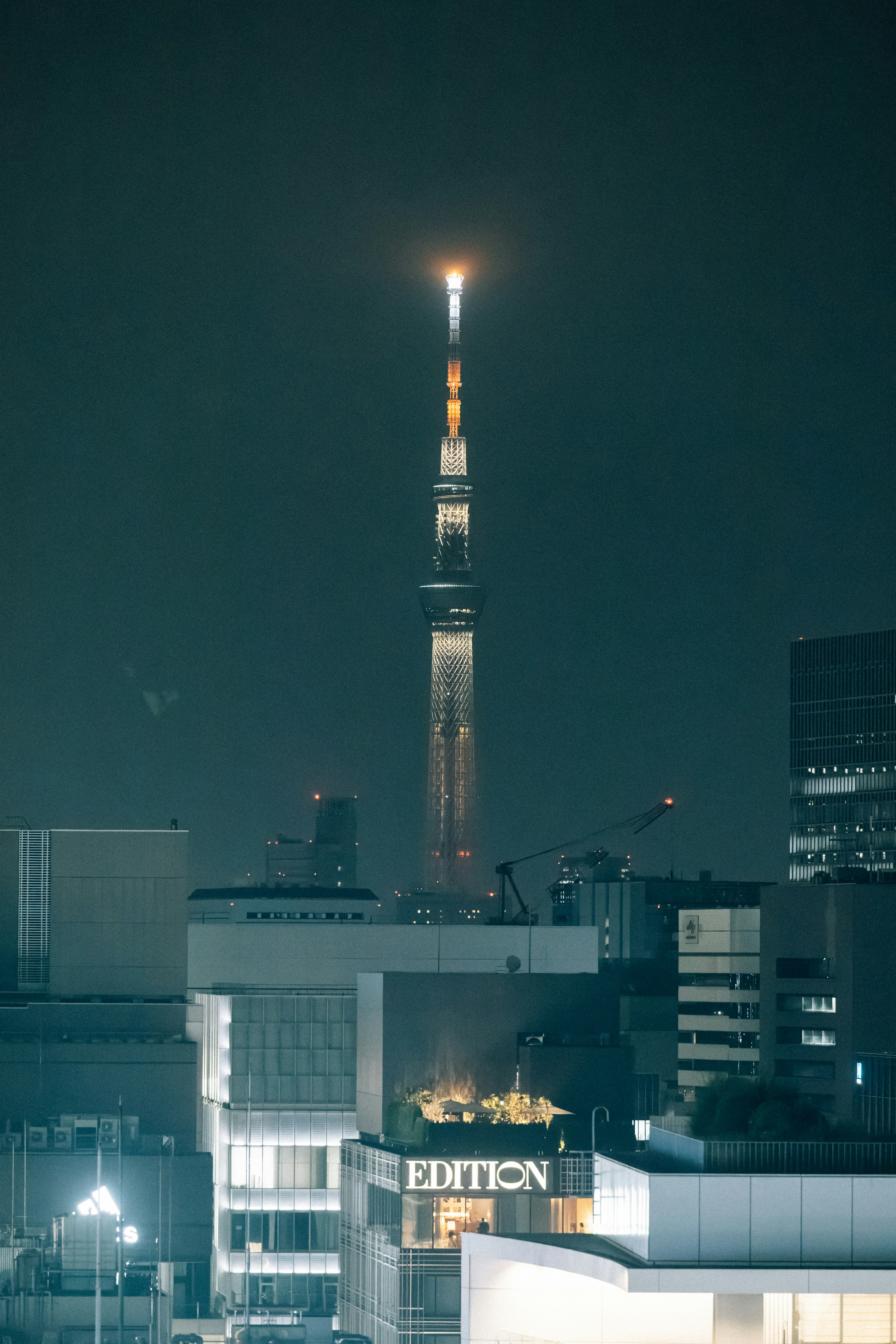 Tall illuminated tower stands above city buildings at night.