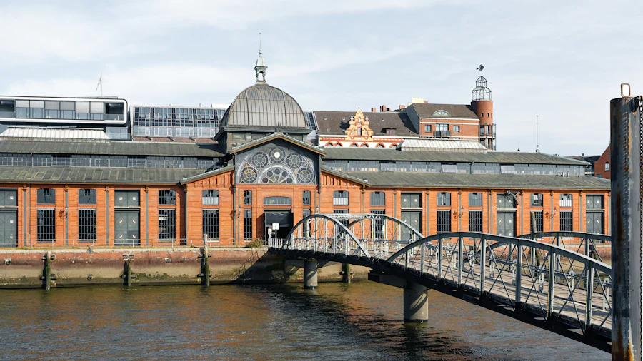 Die Fischauktionshalle in Hamburg-Altona aus rotem Backstein mit Kuppel, davor eine Fußgängerbrücke über das Wasser