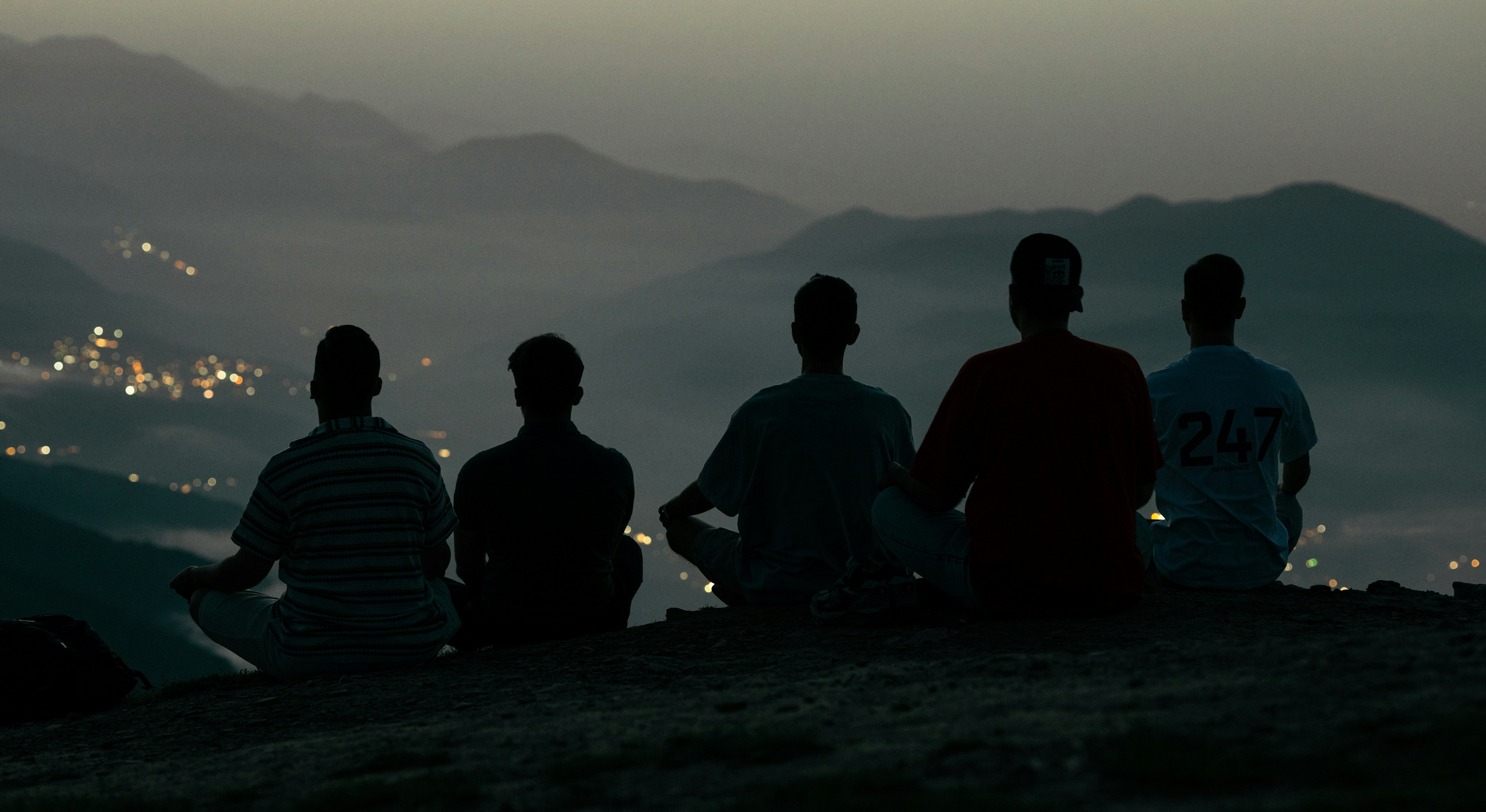 A group of worried Indian expatriates gathered, discussing news on their phones, with a backdrop of an Omani city street.