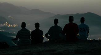 Five people sit on a hilltop overlooking a distant city.