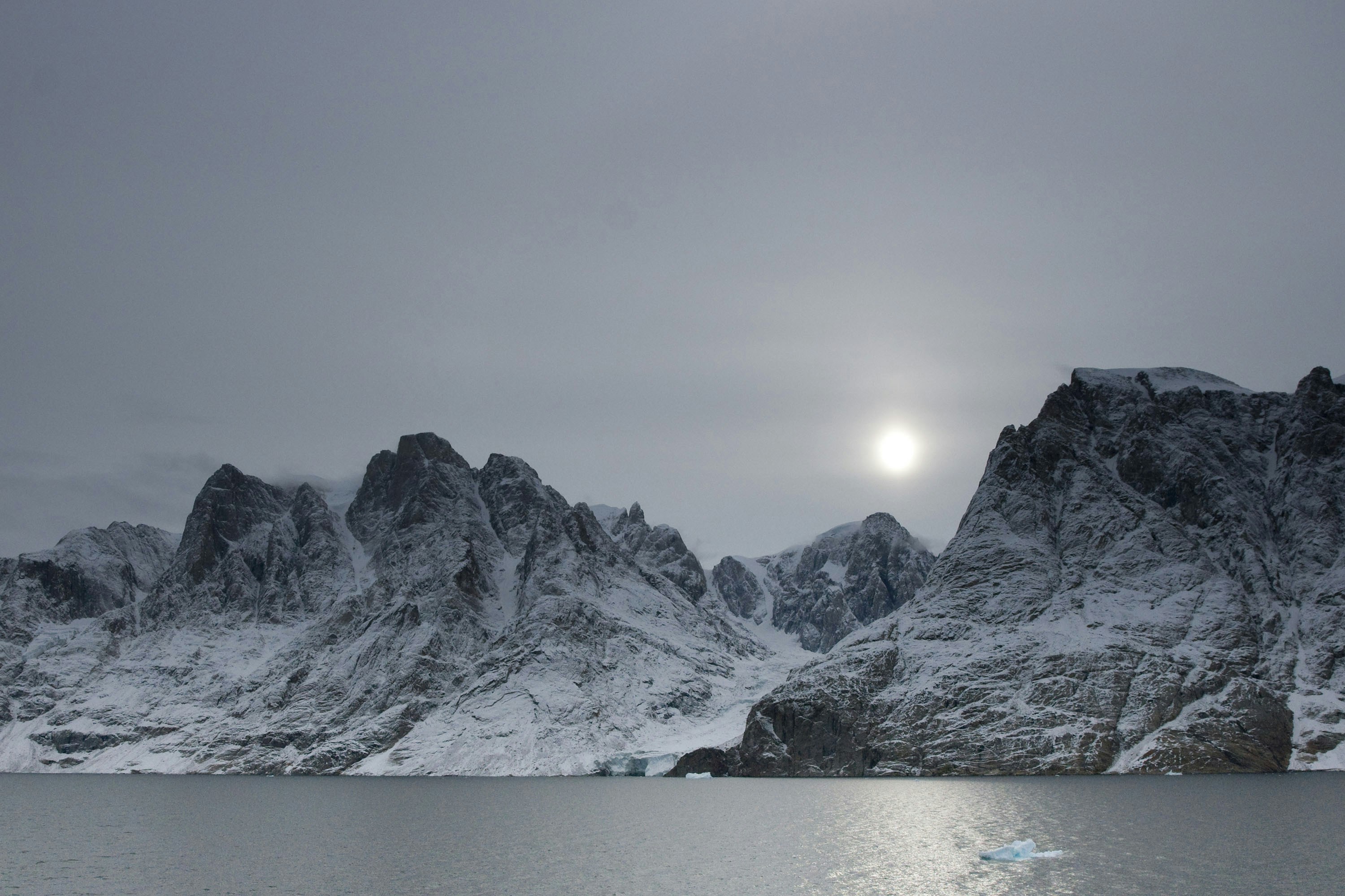Snow-covered mountains rise above a calm, reflective body of water.